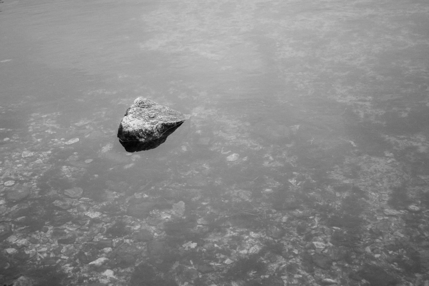 Single dark rock resting on frozen icy surface in black and white minimalist photography.