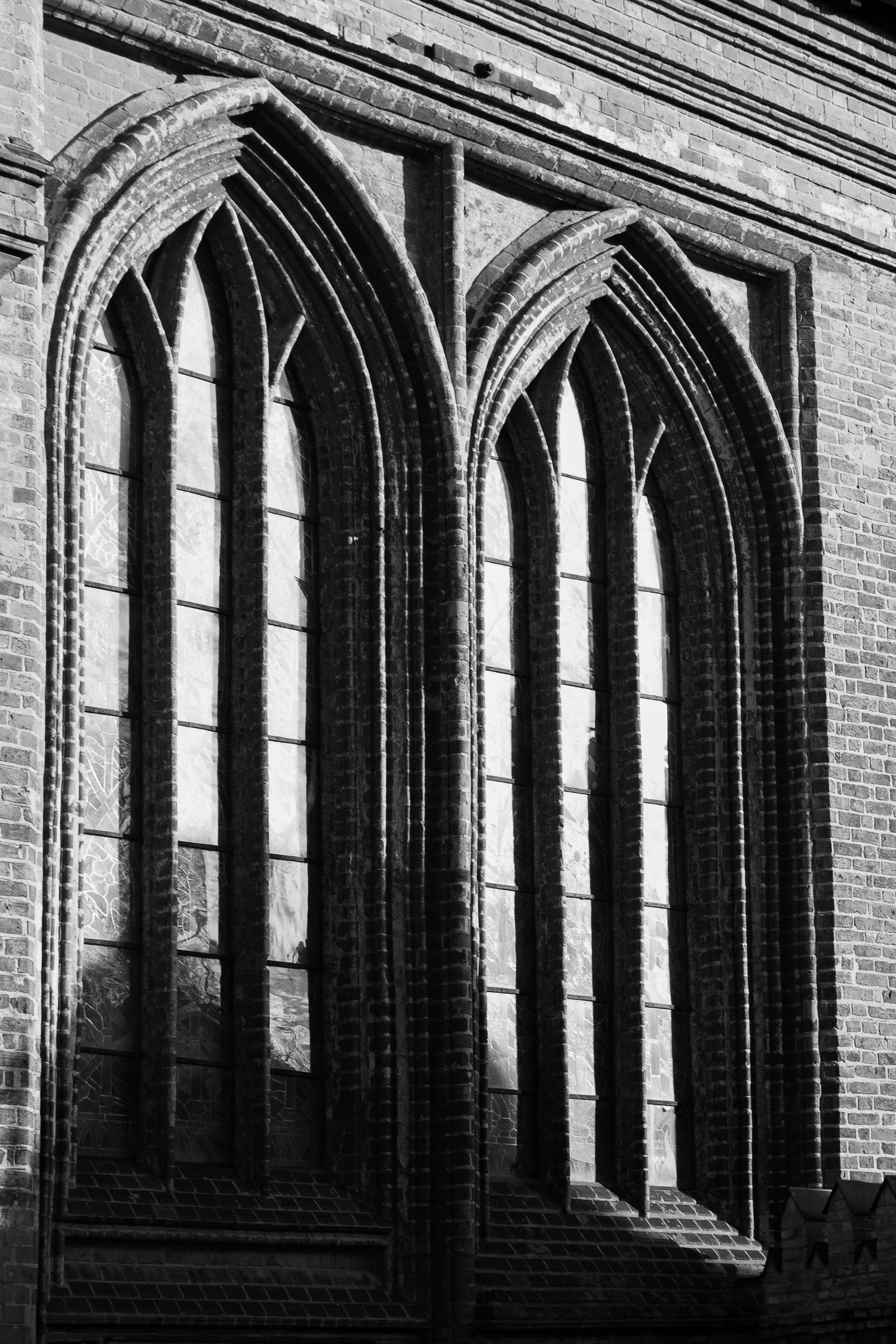 A black and white architectural photo of tall Gothic arched windows on a historic brick cathedral exterior.