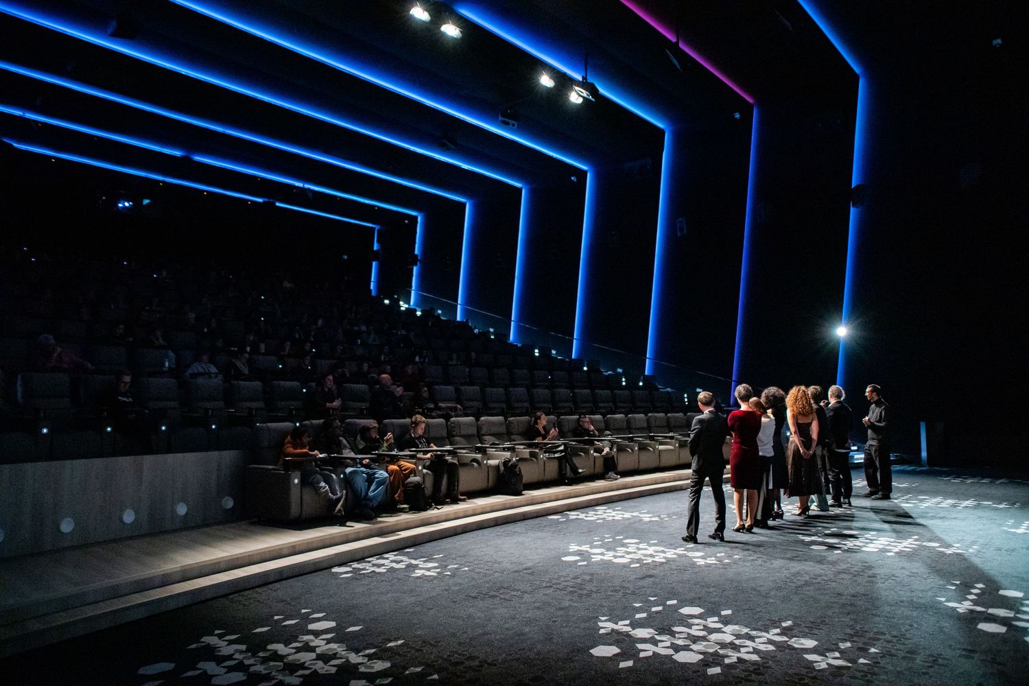 Modern theater auditorium with blue geometric lighting and a small group standing near the stage.