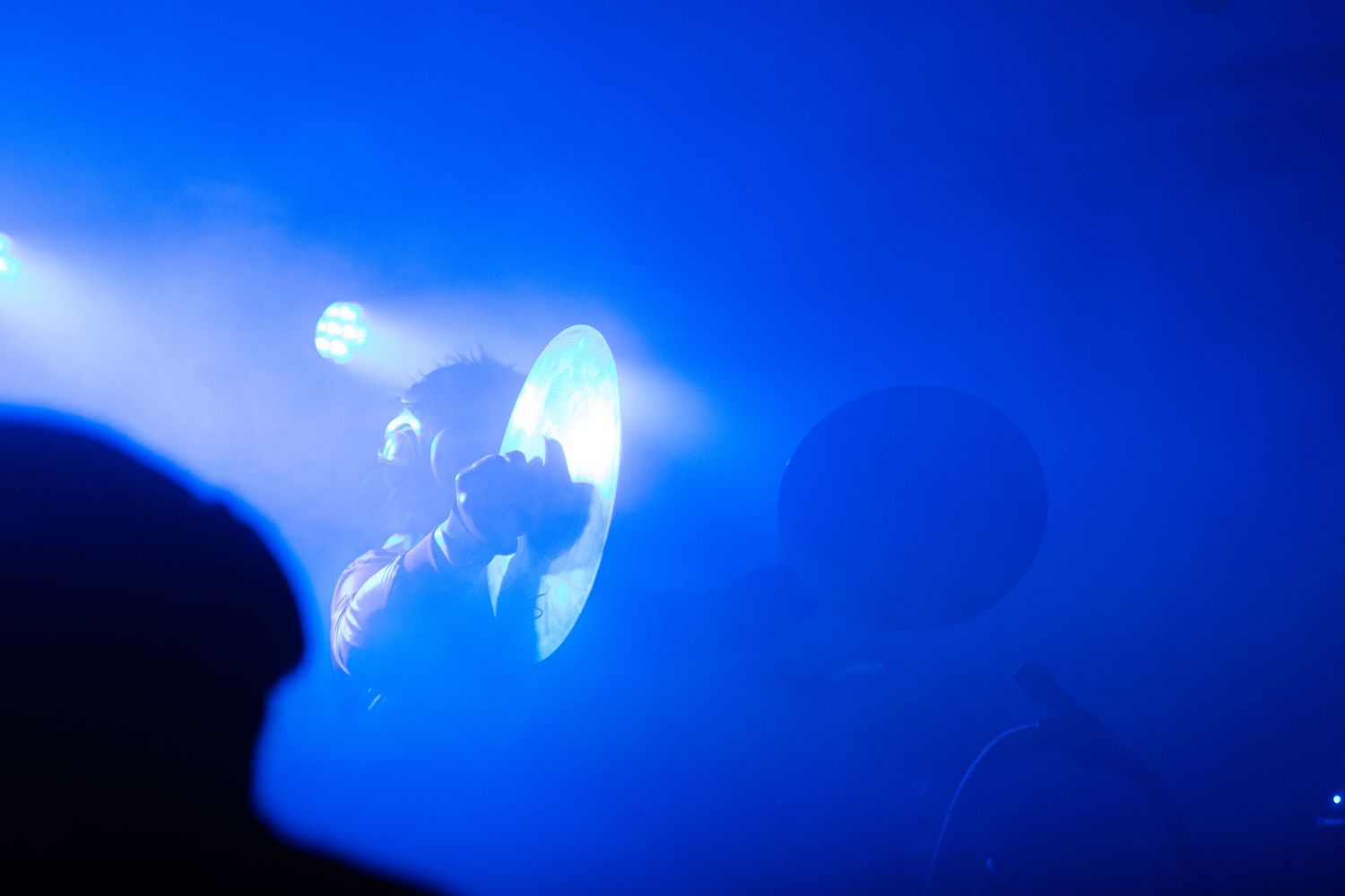 Musician performing on stage under dramatic blue spotlight with foggy atmosphere at a live concert.