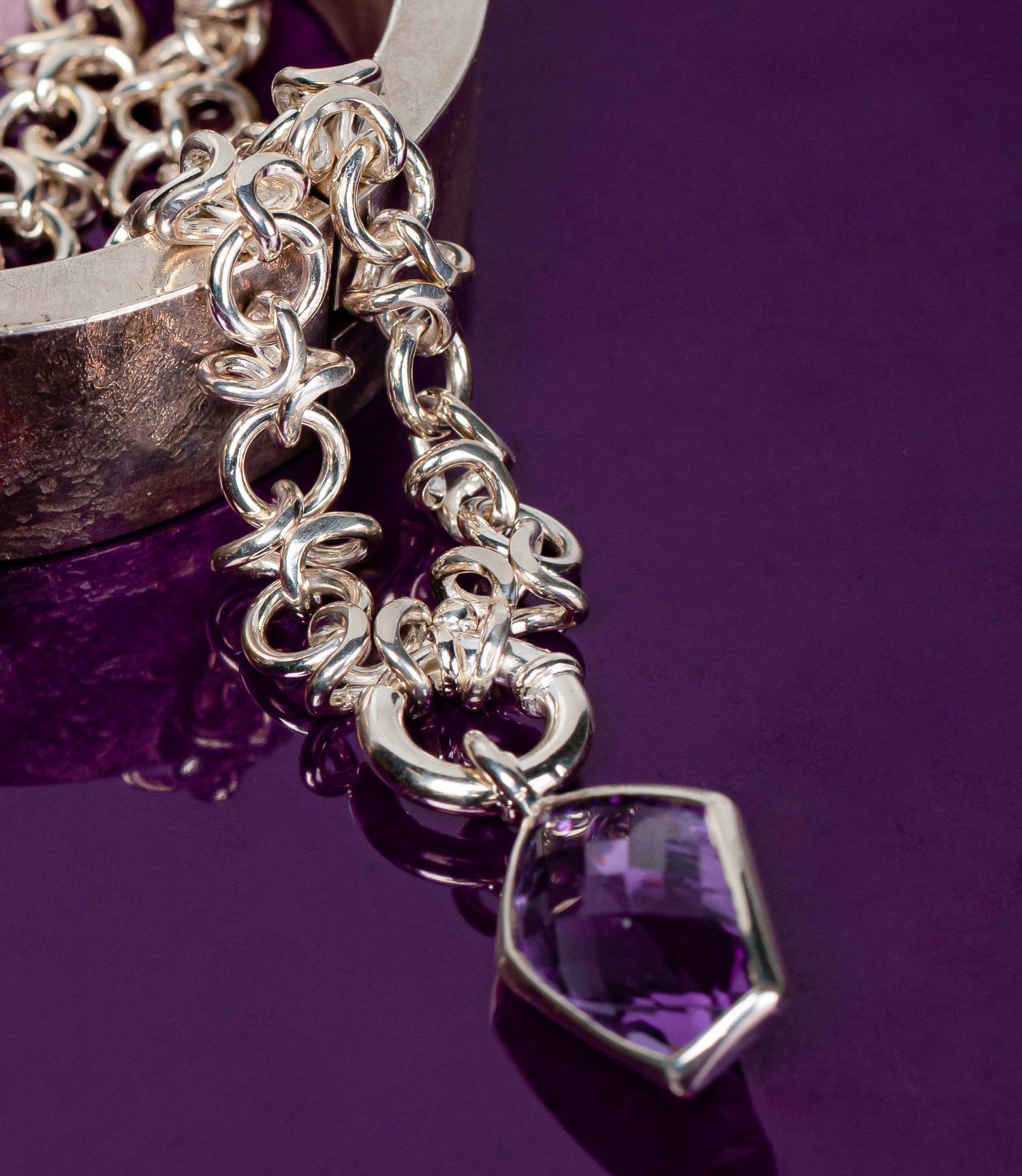 Silver chainmail necklace with a faceted amethyst pendant on a purple background.