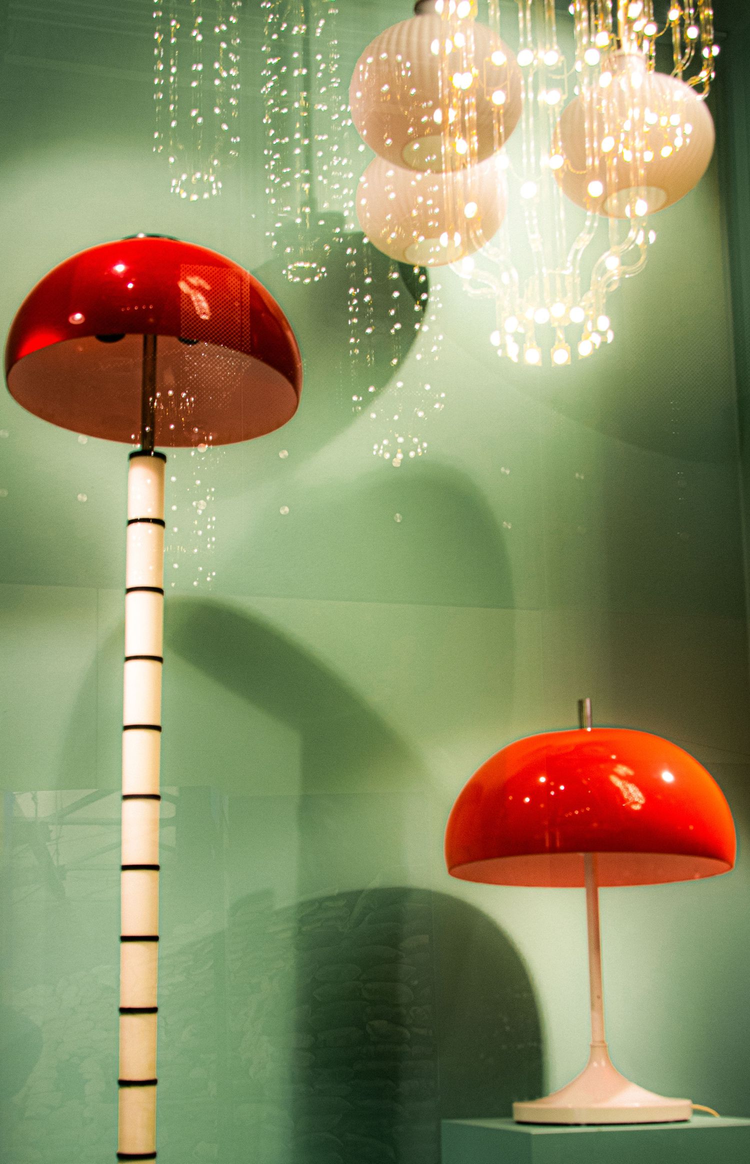 Retro red mushroom-shaped floor and table lamps displayed against mint green wall with crystal chandelier above.