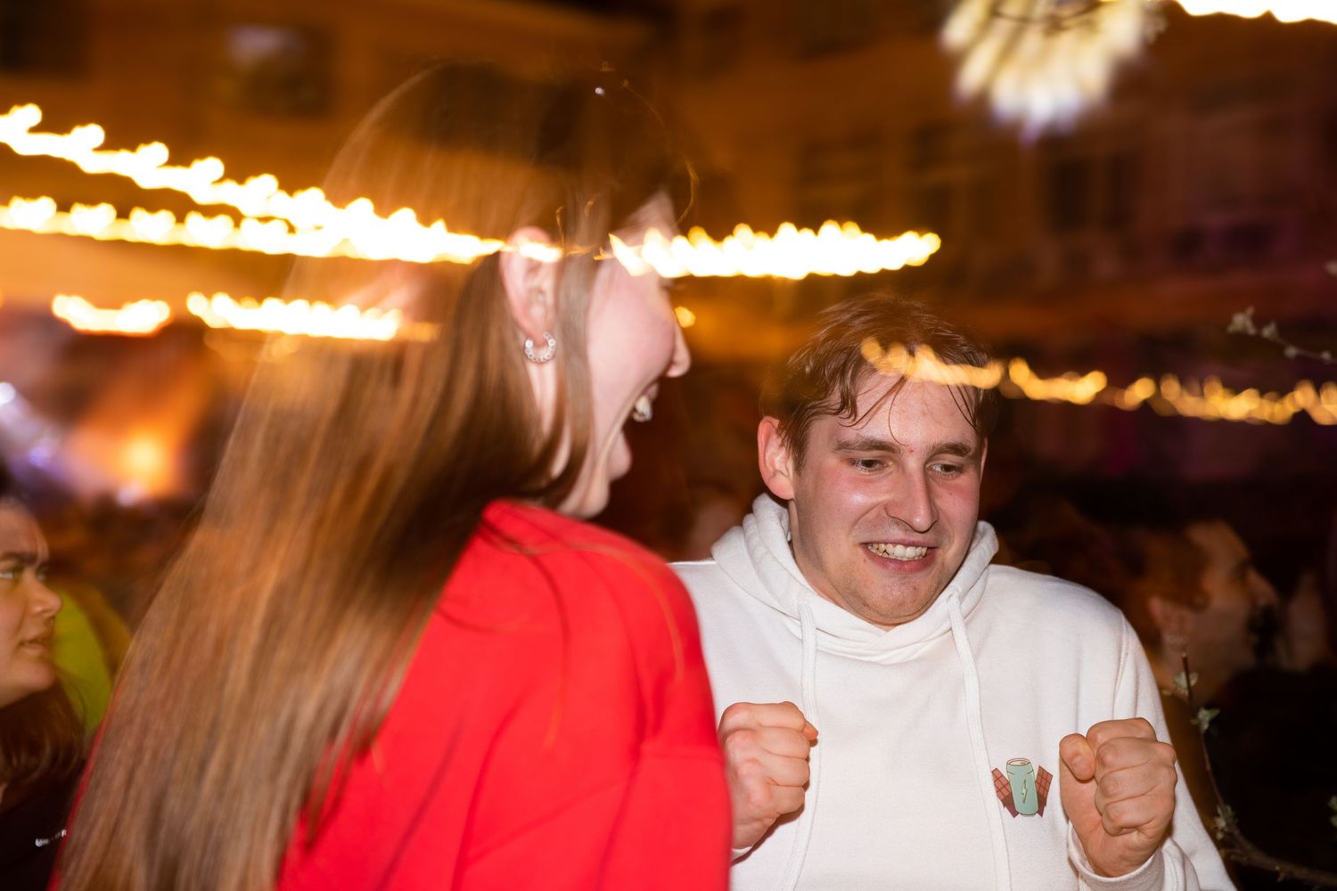 Young couple laughing and celebrating together under golden lights at a festive outdoor event.