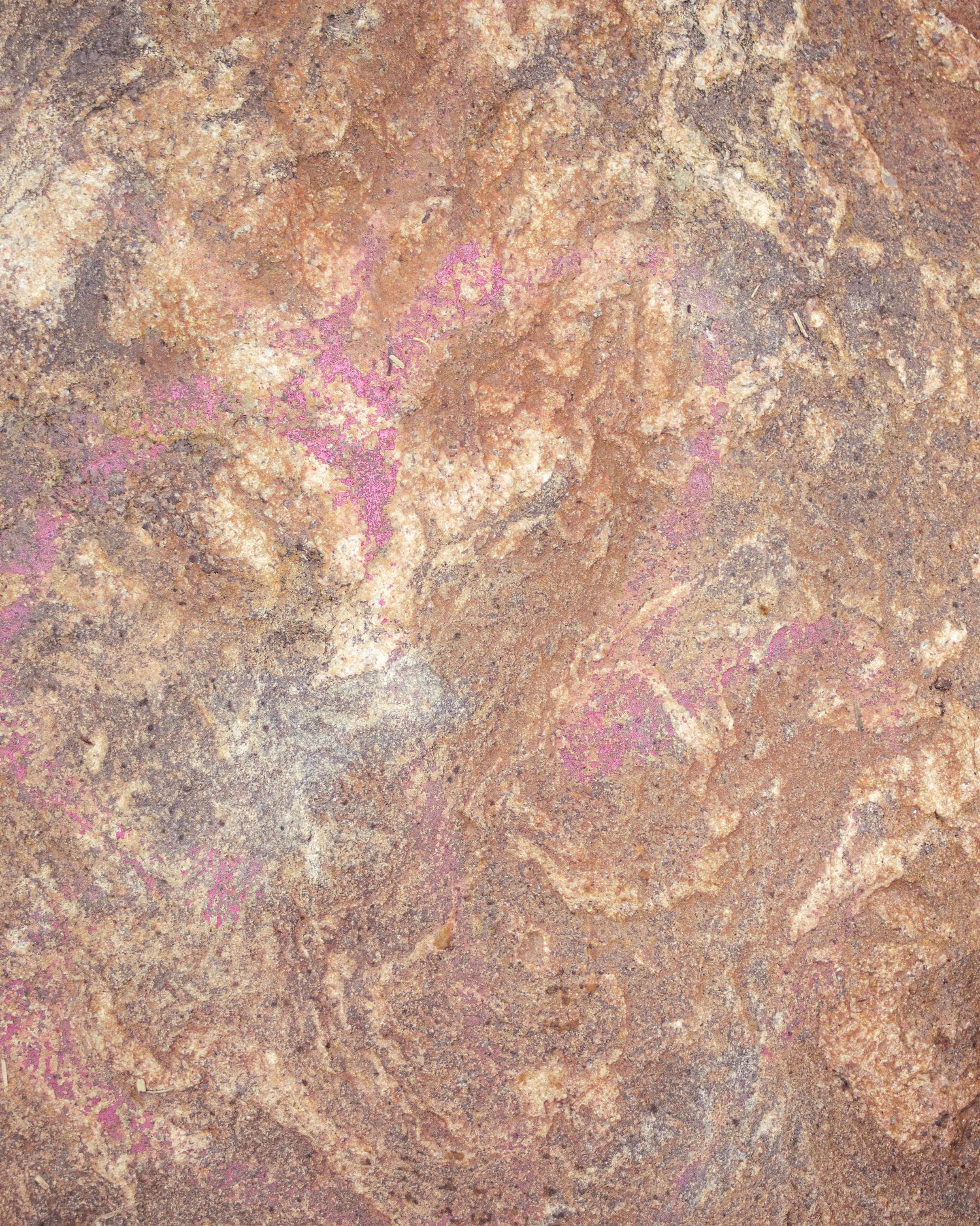 Close-up texture of rough stone surface with pink and gold mineral veins and earthy tones.