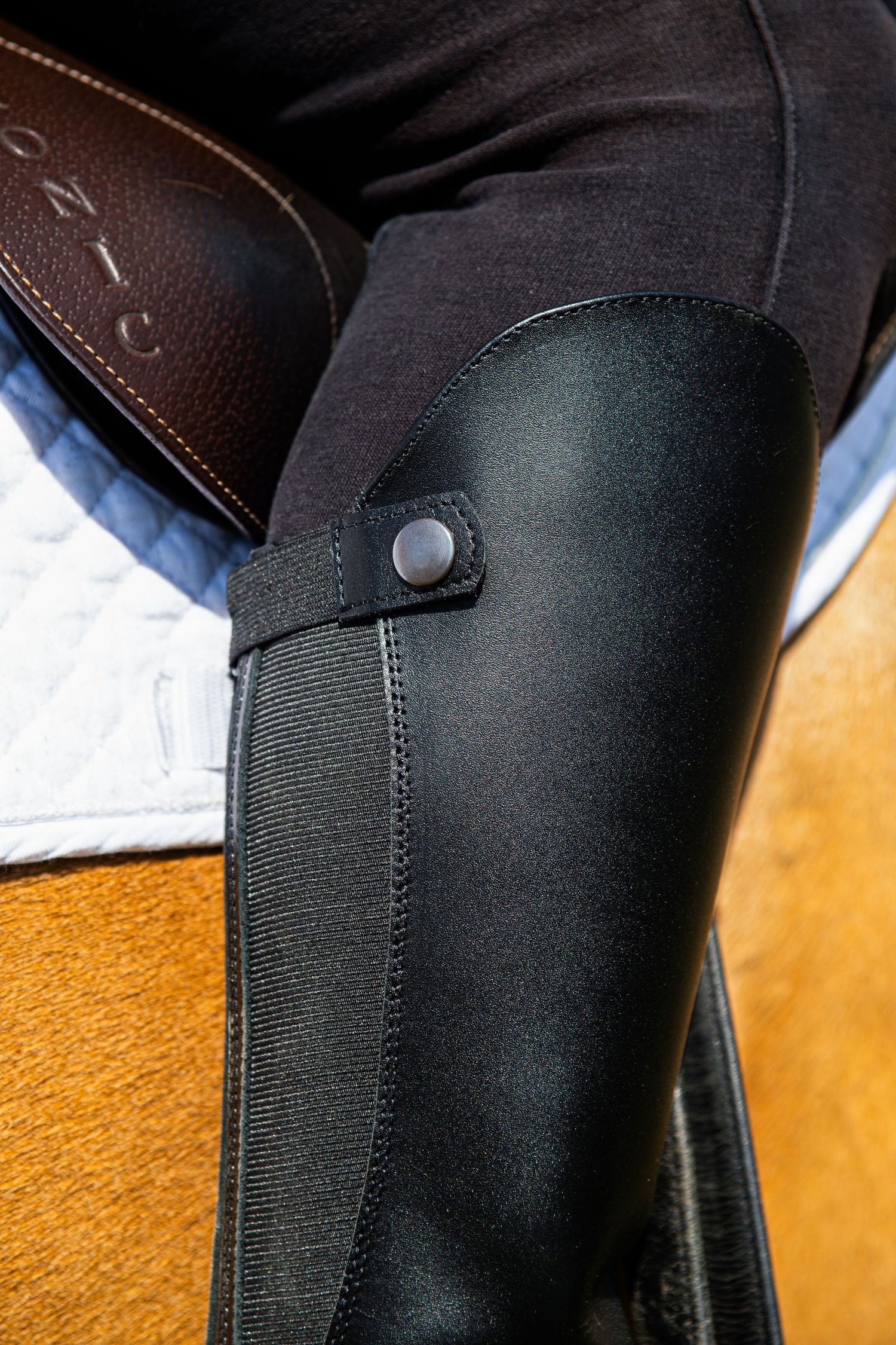 Close-up detail of black leather equestrian riding boot with elastic panel while mounted on horse.
