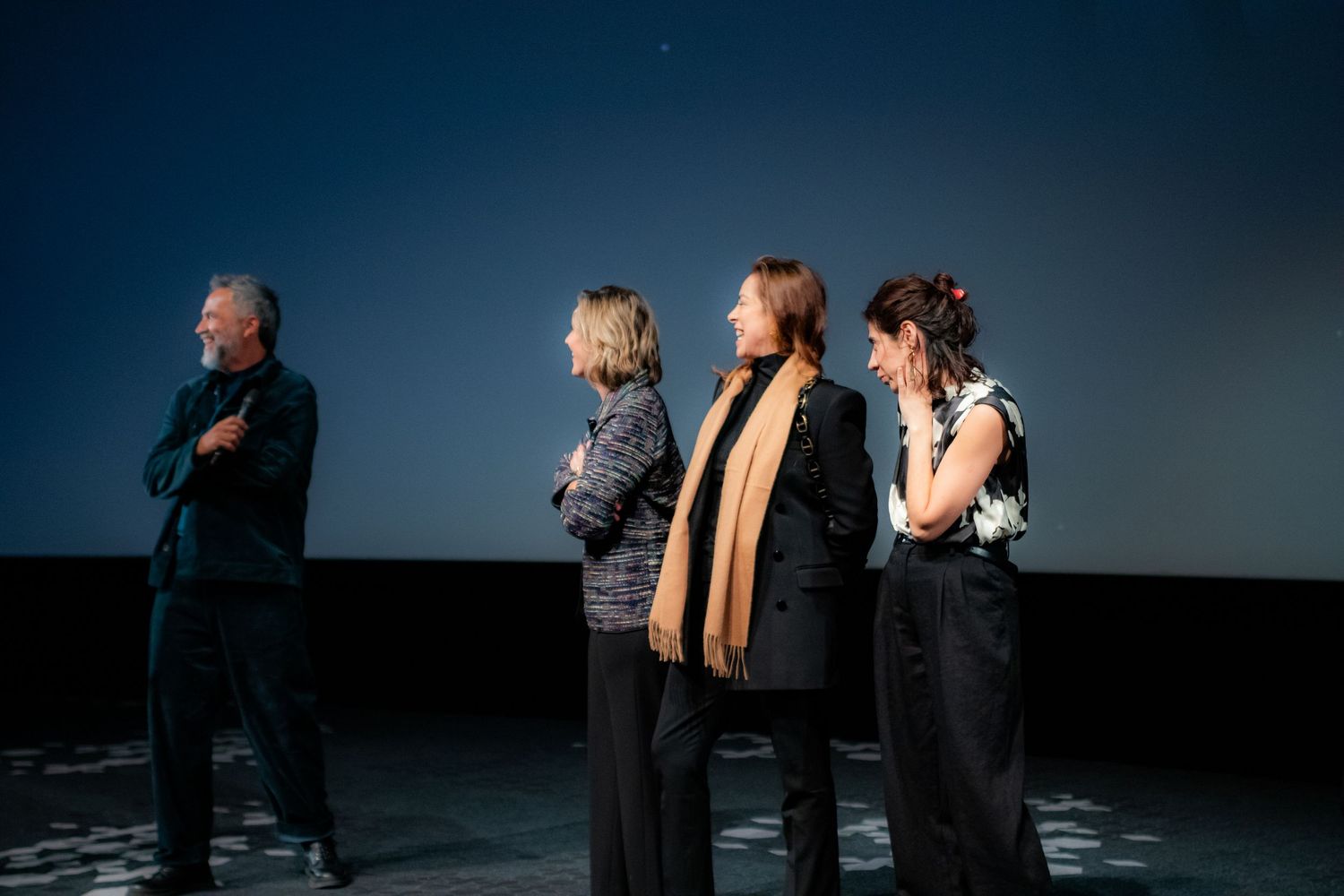 Four people stand on a cinema stage in front of a starry blue projected backdrop during a film festival event.