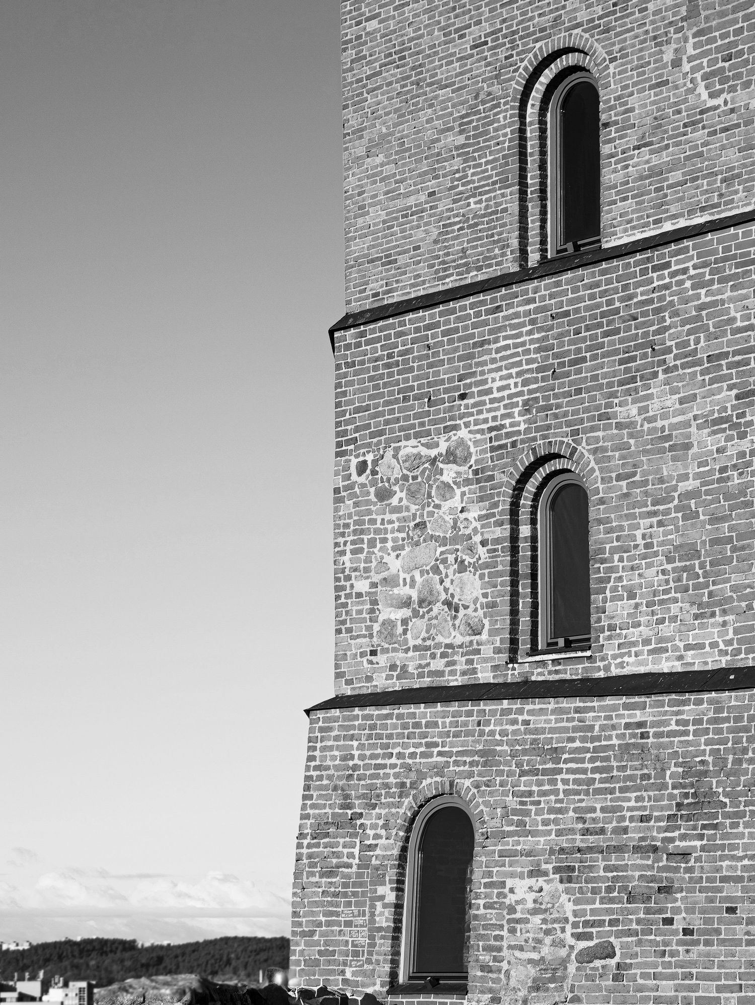 Black and white photo of a brick church tower with arched windows against a clear sky.