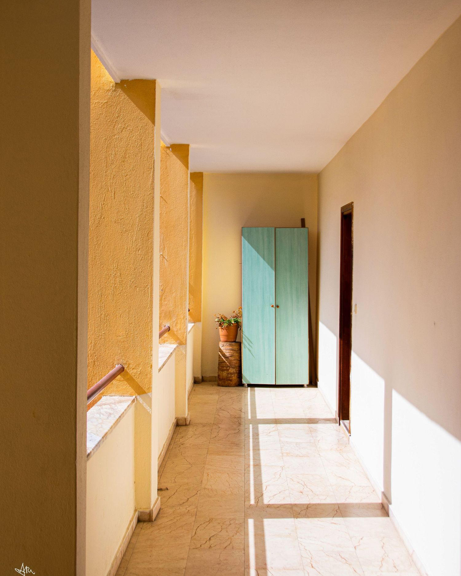 Sunlit interior hallway with yellow walls, marble floors, and a turquoise cabinet at the end.