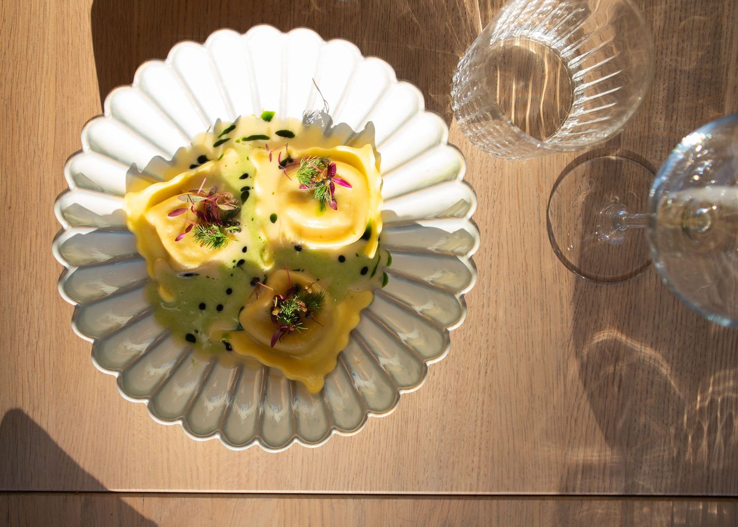 Yellow ravioli pasta with edible flowers and herbs on decorative white scalloped plate.