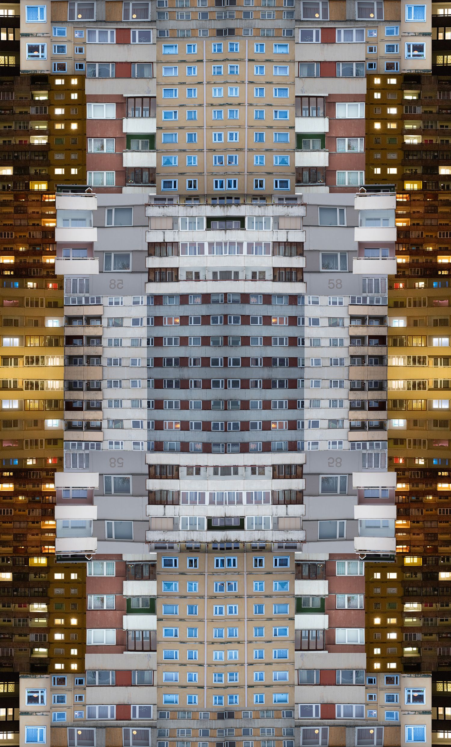 Symmetrical mirrored facade of a tall residential apartment building with illuminated windows at night.