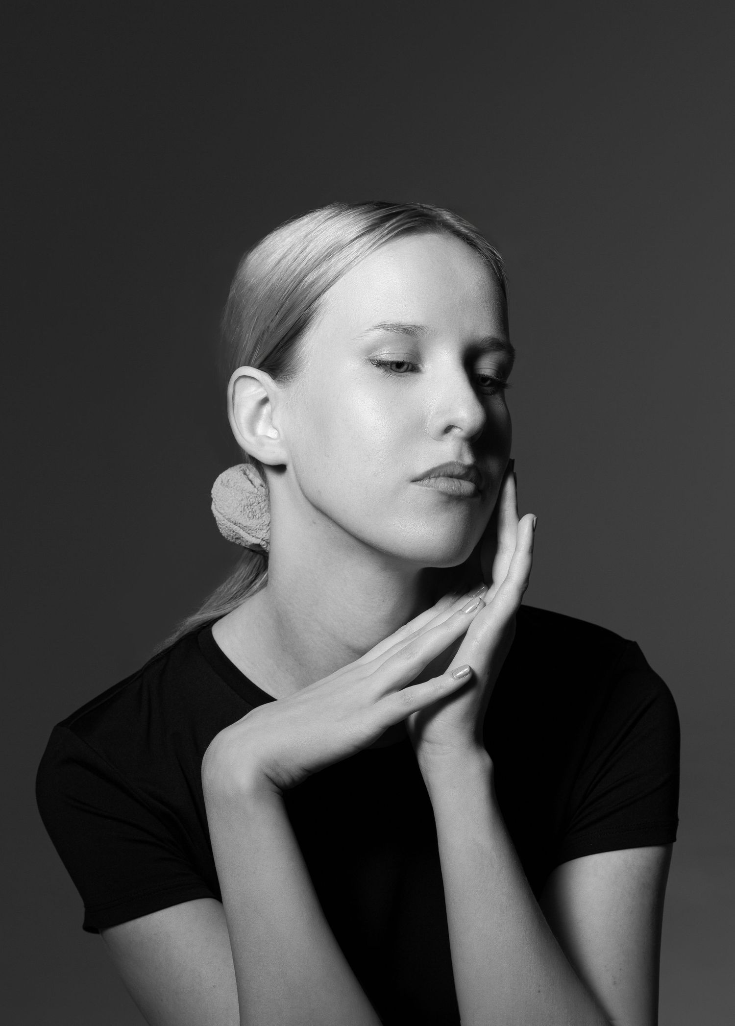 Black and white studio portrait of blonde woman with hands clasped near face.