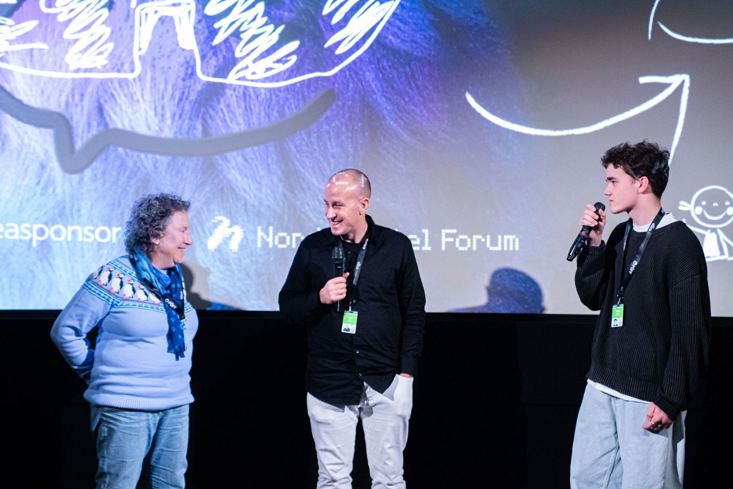 Three people speaking on stage at a film festival Q&A session with microphones.