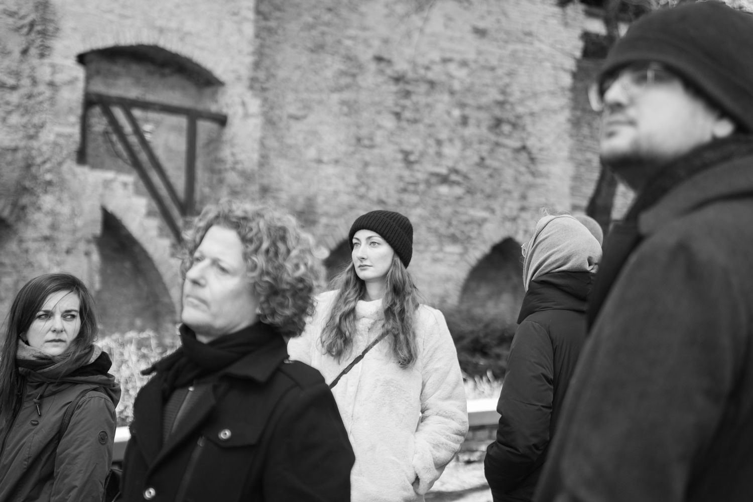 A group of four people stand outdoors near ancient stone ruins on a cloudy day.