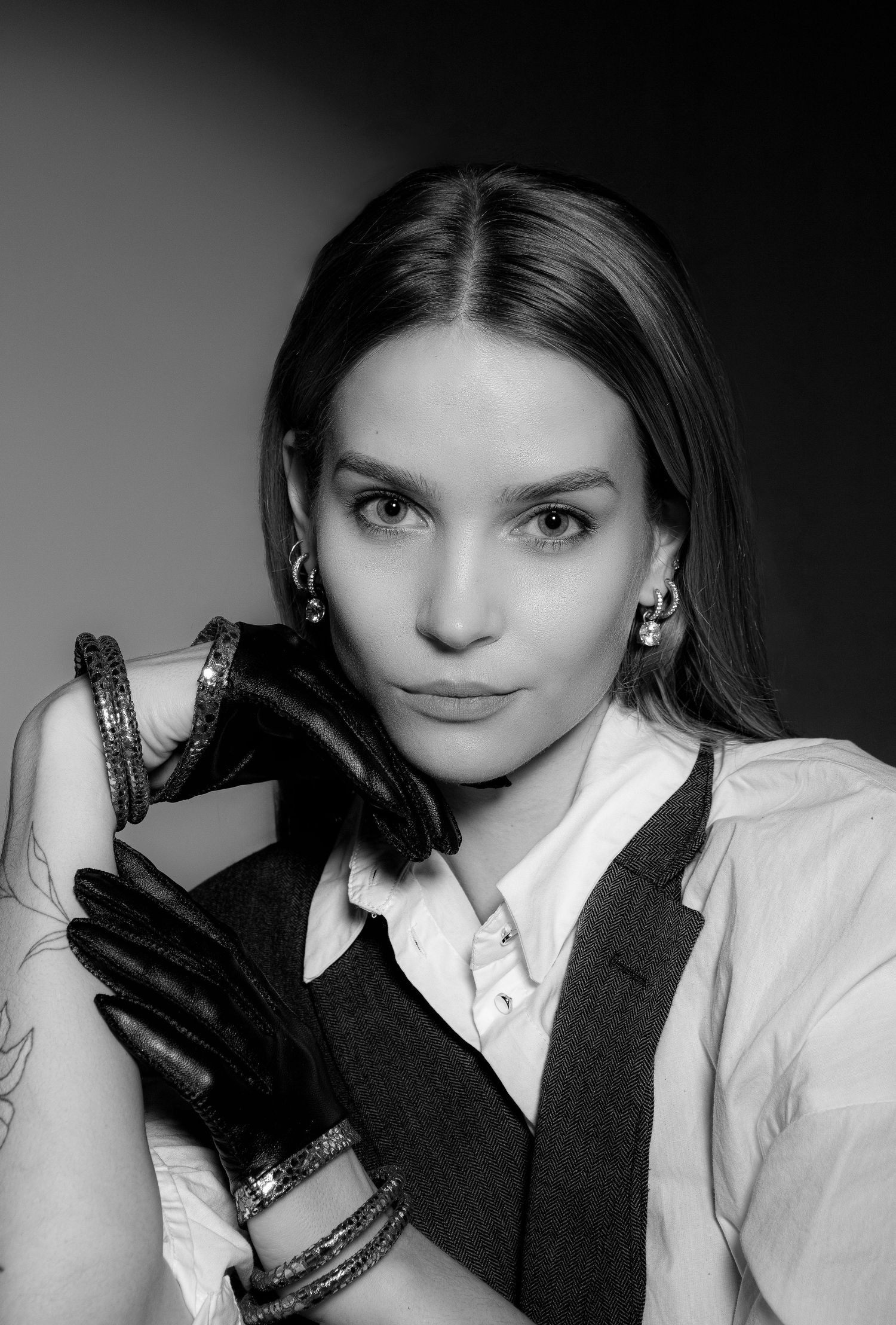 Black and white portrait of brunette woman in vest and leather gloves with bracelets and tattoos.