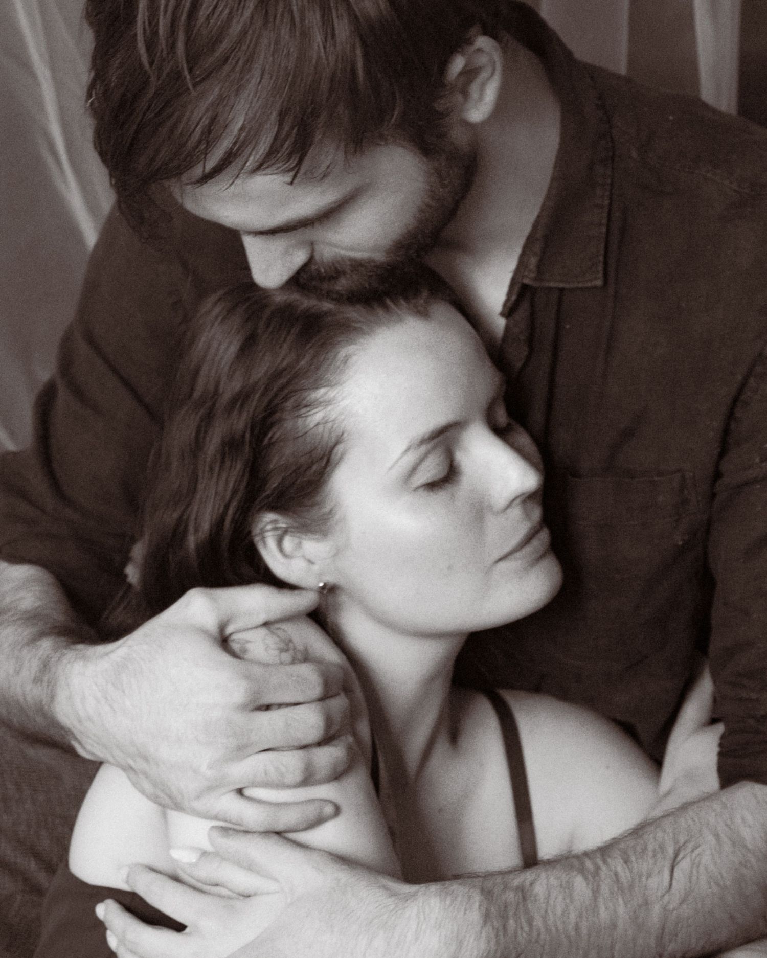 Black and white photo of a couple embracing tenderly, man holding woman from behind in an intimate portrait.