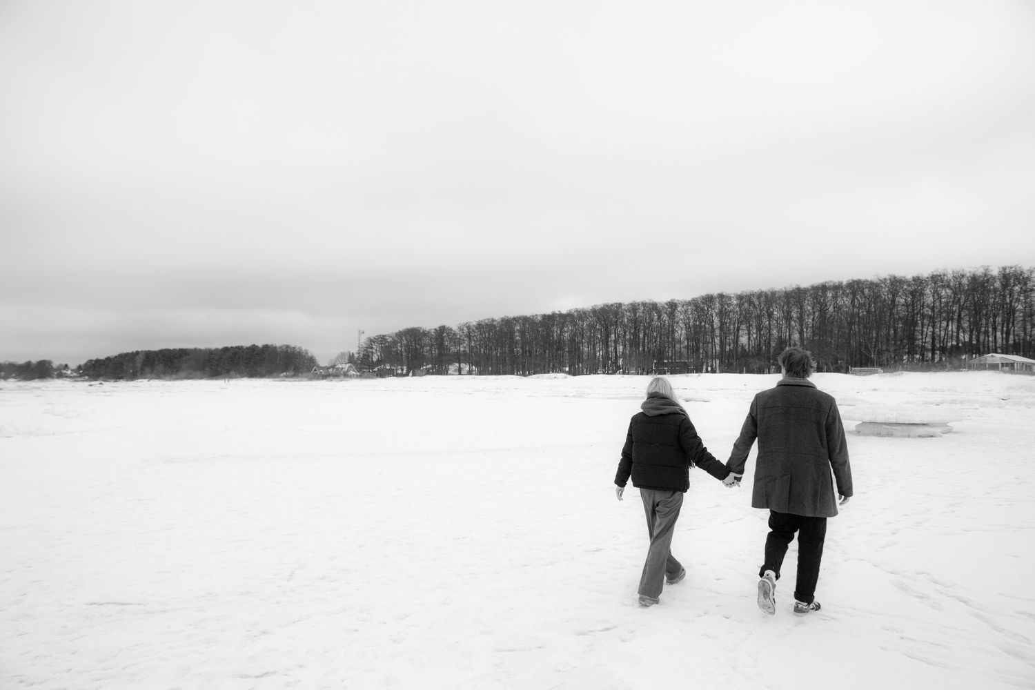 Couple holding hands walking across a snowy frozen lake in winter, black and white photography.