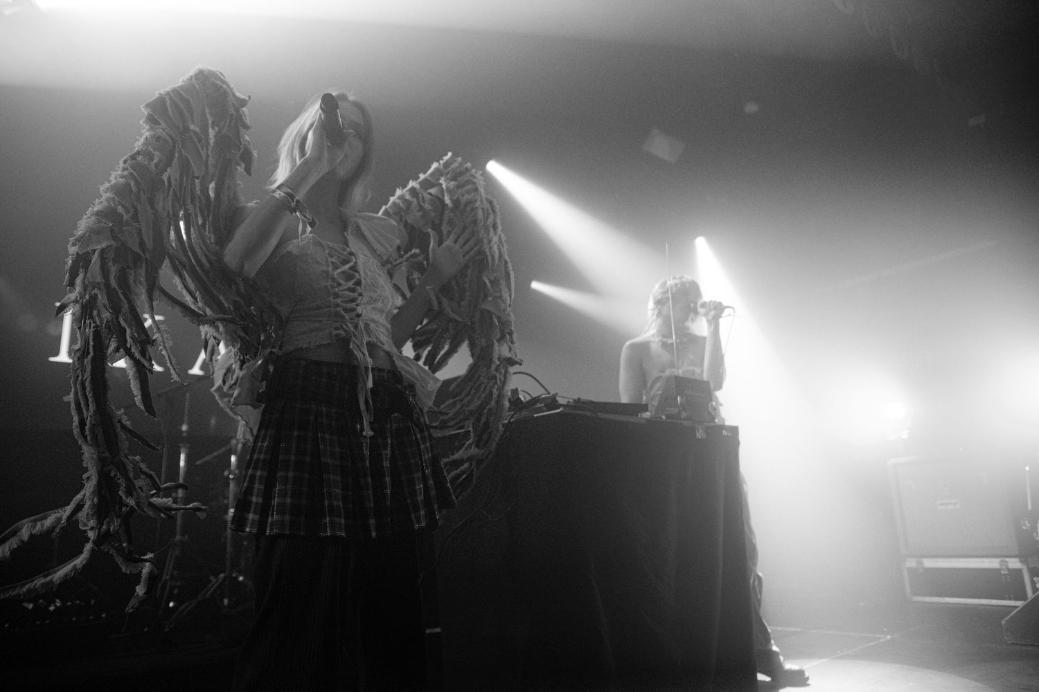 Black and white photo of performers in elaborate costumes on a dramatic stage with bright spotlights.