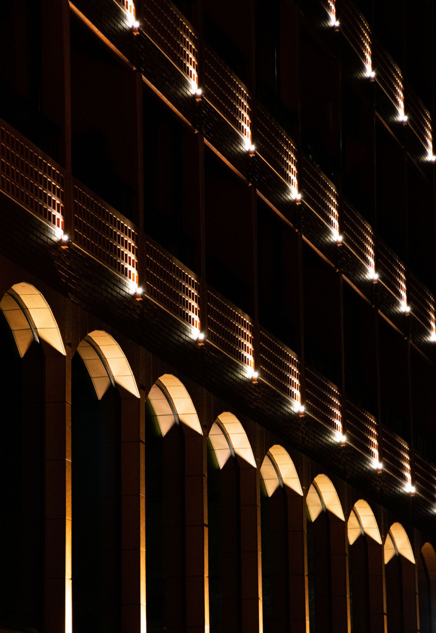 Illuminated arched windows and rows of lights on a dark building facade at night.