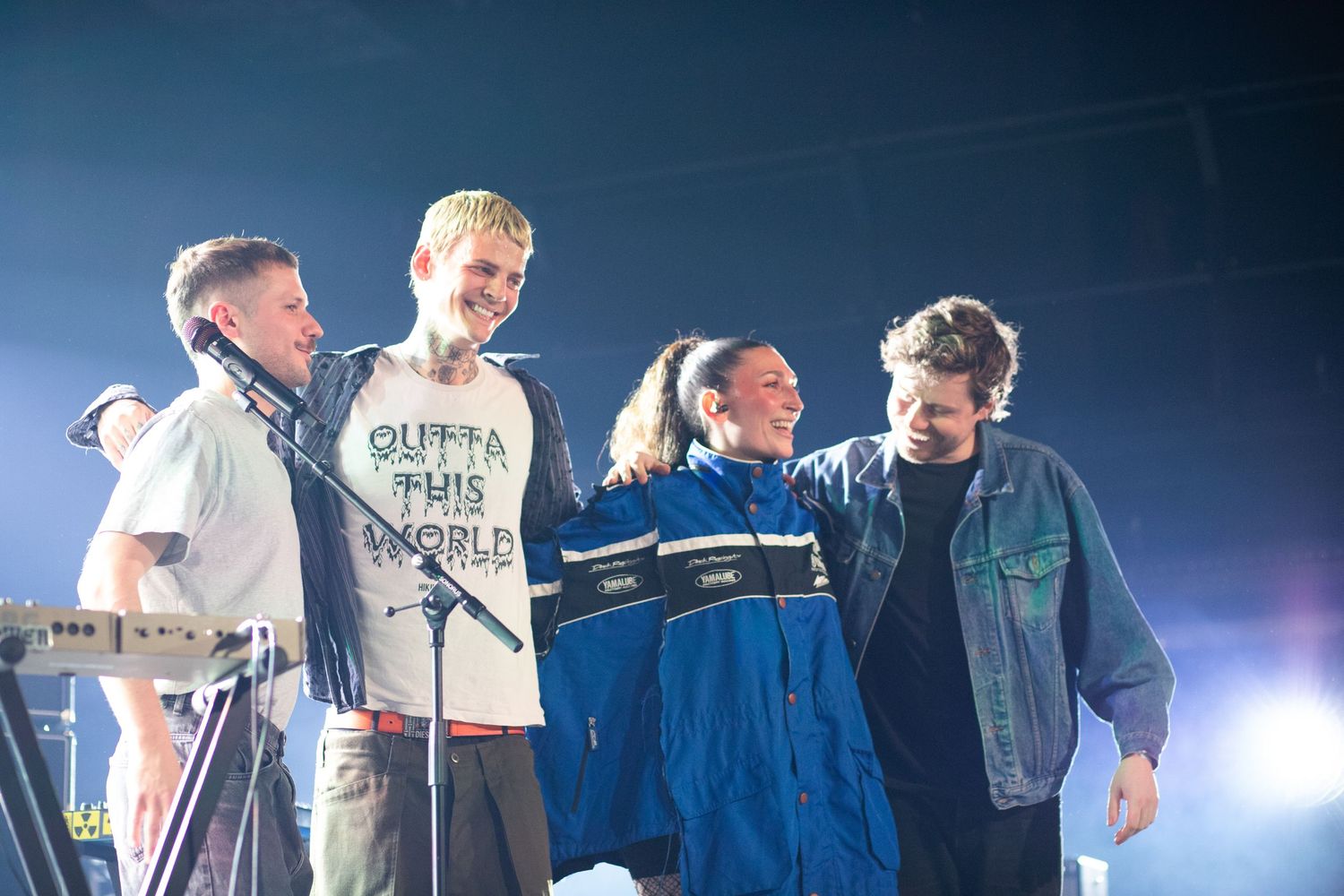 Four band members posing together smiling on stage after a live concert performance.