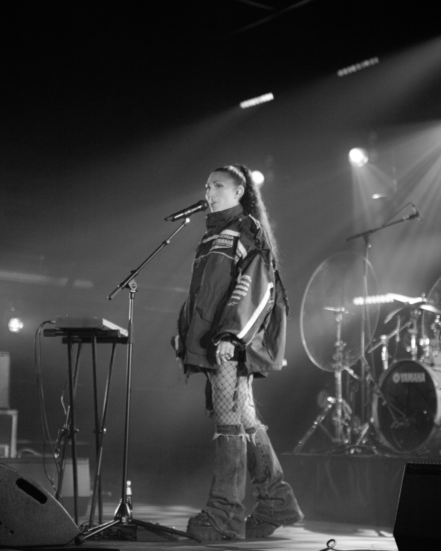 Black and white image of a female artist singing on stage with dramatic beam lighting behind her.