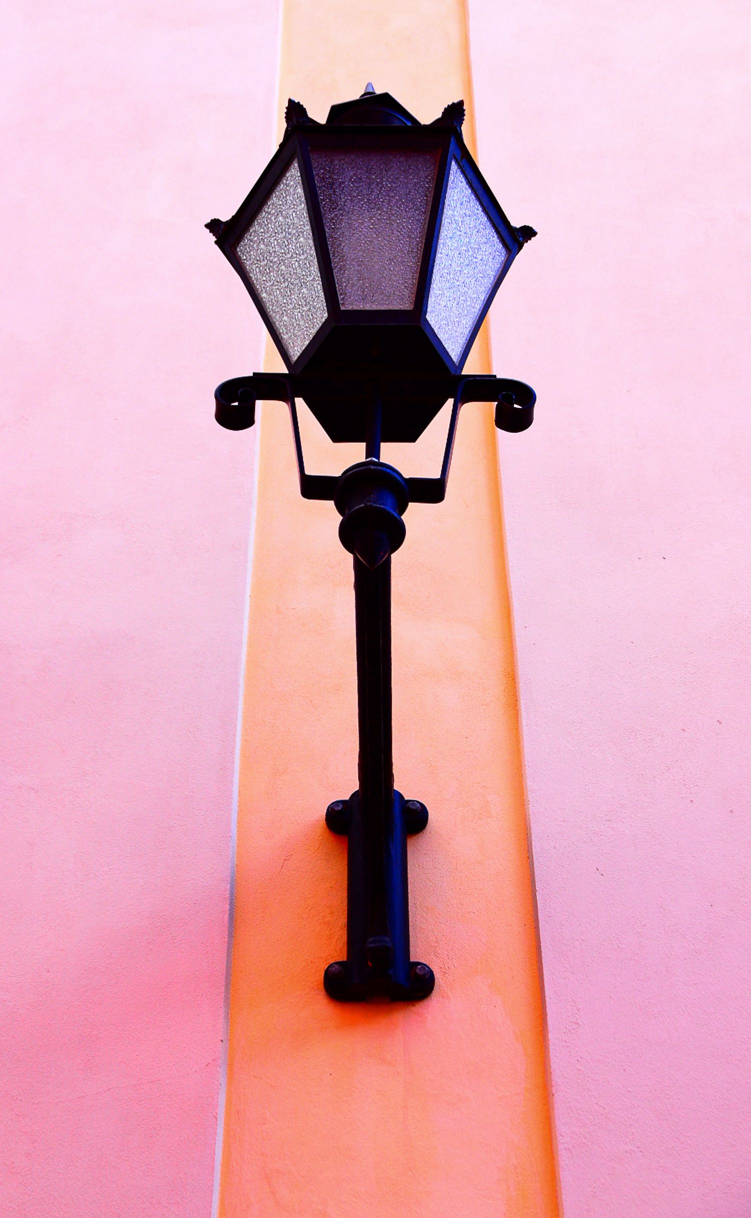 Black ornate vintage street lamp mounted on a pink and peach wall corner.