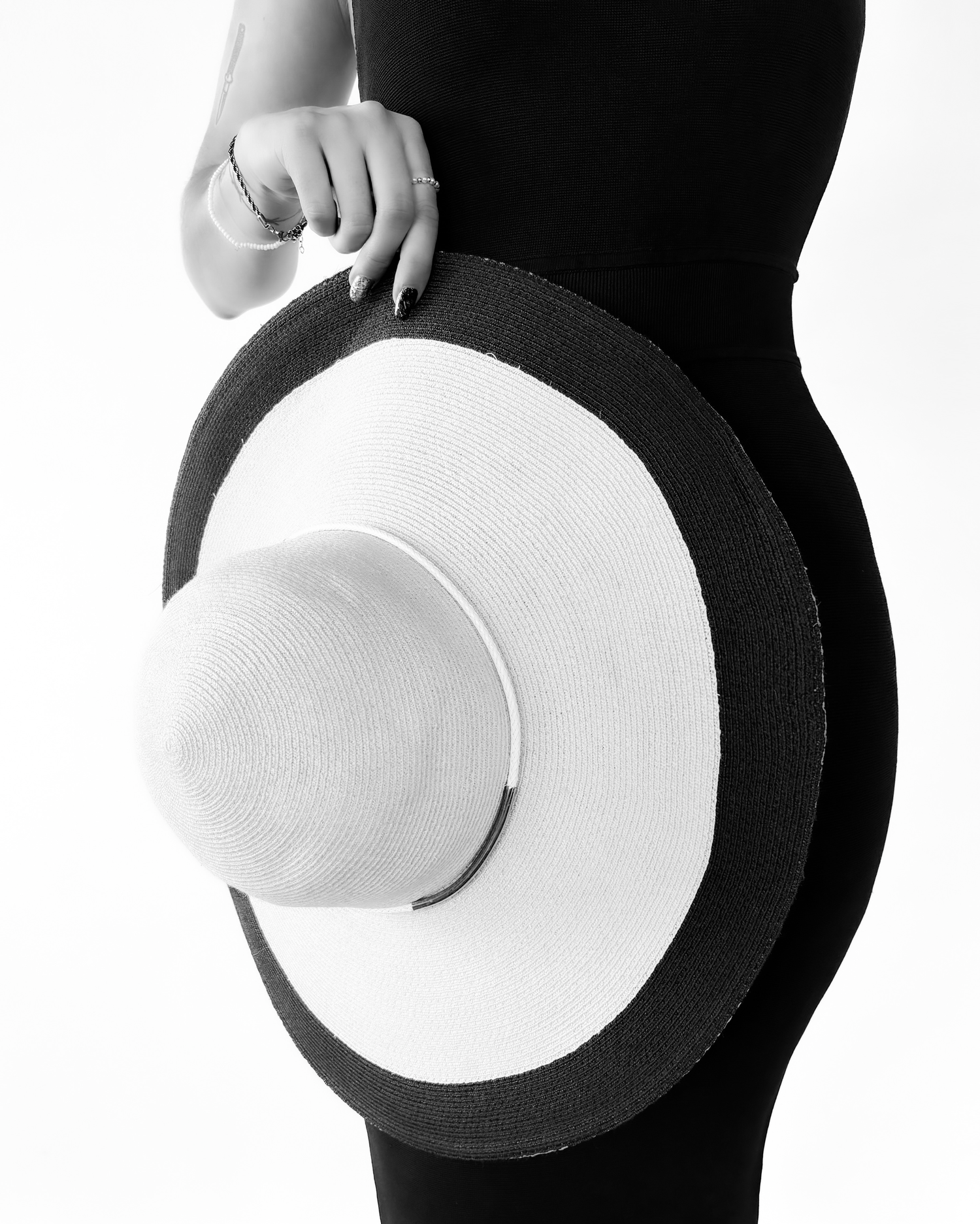 Black and white photo of a woman in a black outfit holding a wide-brim sun hat with dark trim.