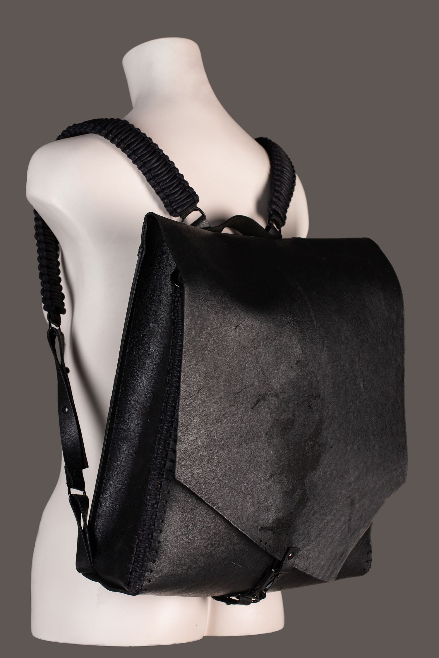 Black leather backpack with braided straps displayed on a white mannequin torso.