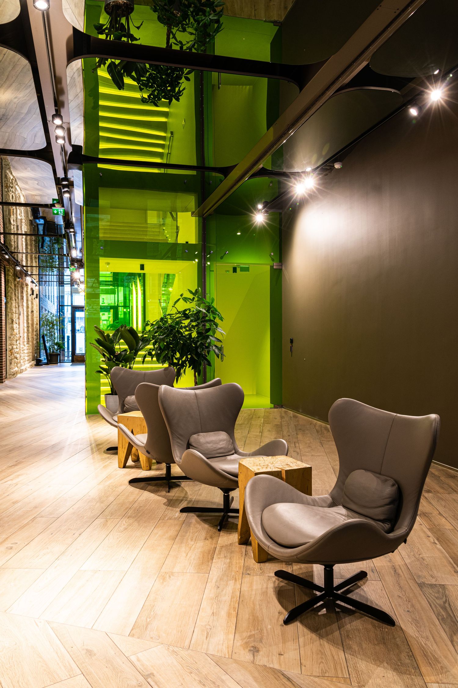 Contemporary lounge area with gray egg chairs, green illuminated glass staircase, and exposed brick wall accents.