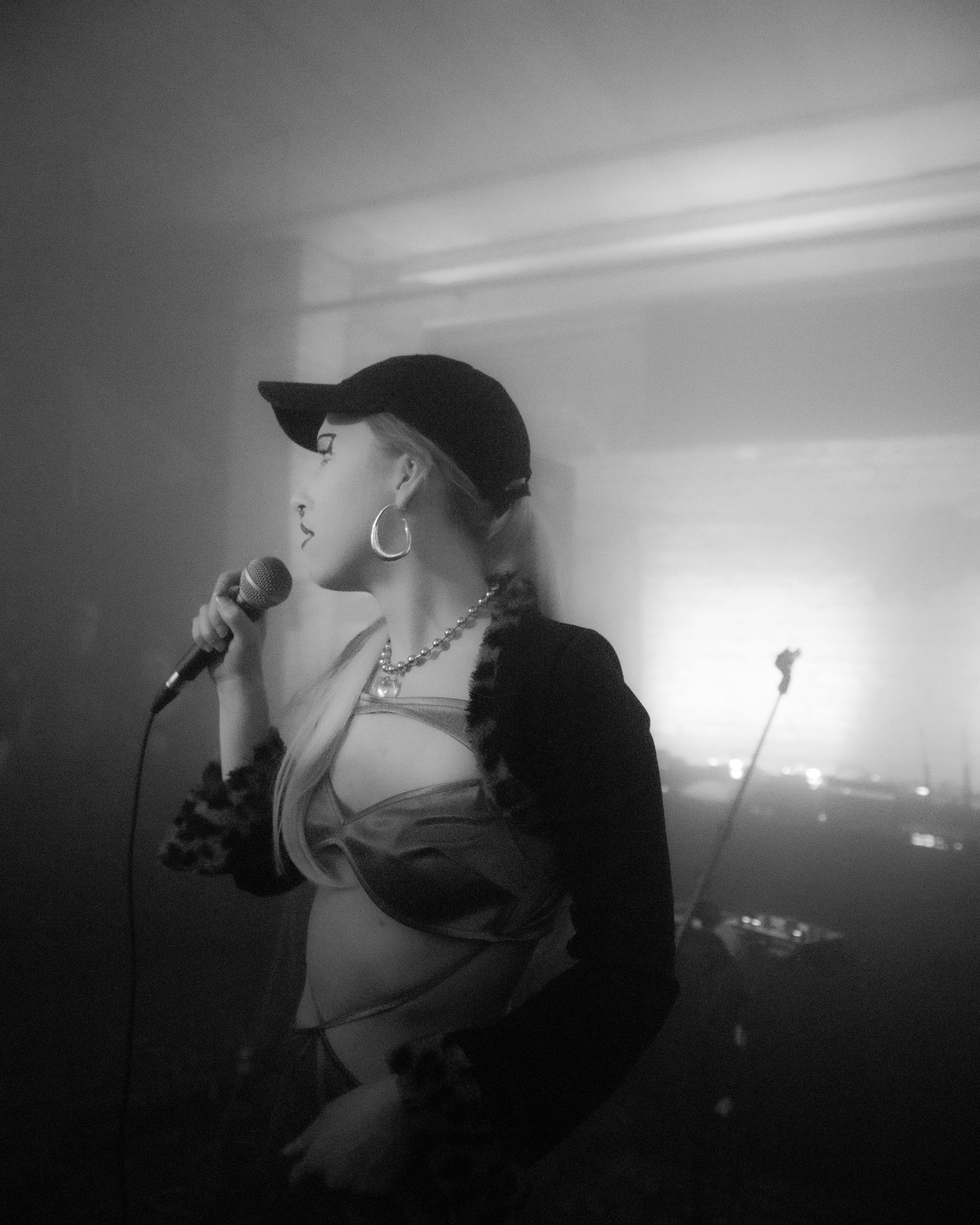 Close-up black and white portrait of a female singer performing with a microphone in a foggy club.
