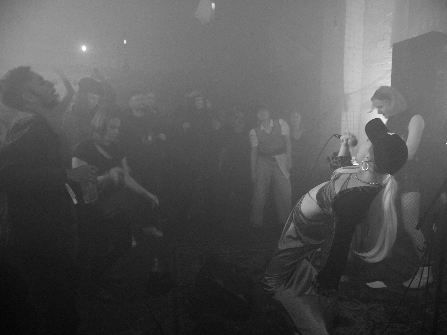 Black and white photo of a crowd of people dancing in a foggy dimly lit venue.
