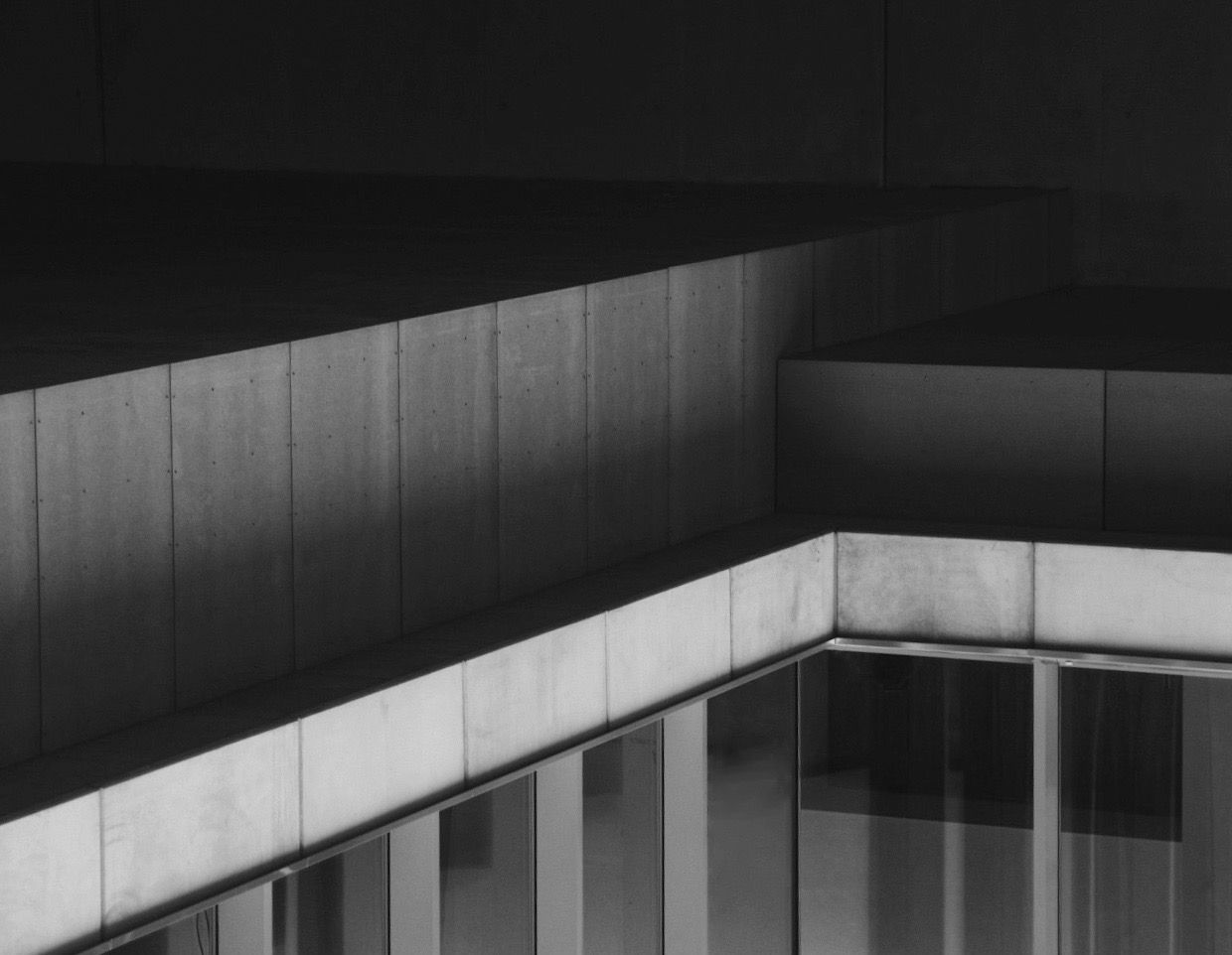 Black and white minimalist architectural detail of concrete building with horizontal ledges and glass panels.