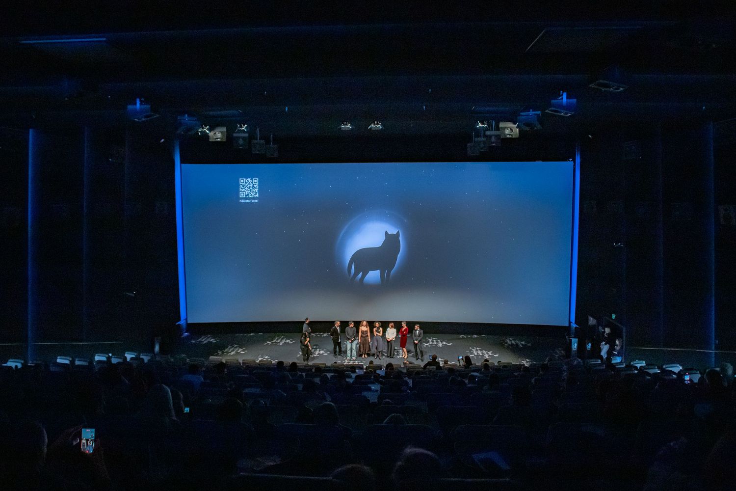 A large cinema audience watches a film premiere with a wolf logo projected on the big screen during an awards ceremony.