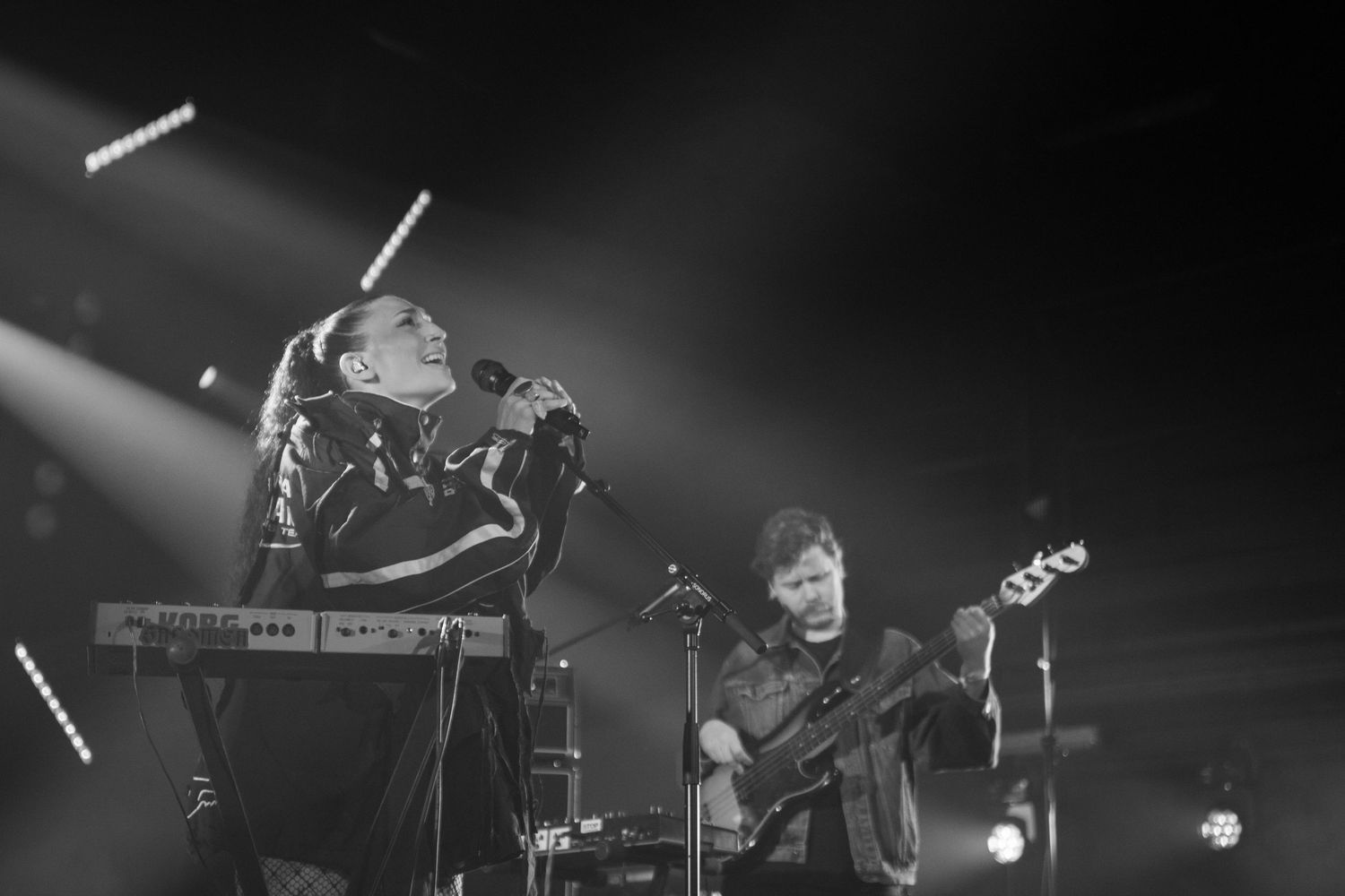Black and white photo of two musicians performing on stage with a keyboard and bass guitar.