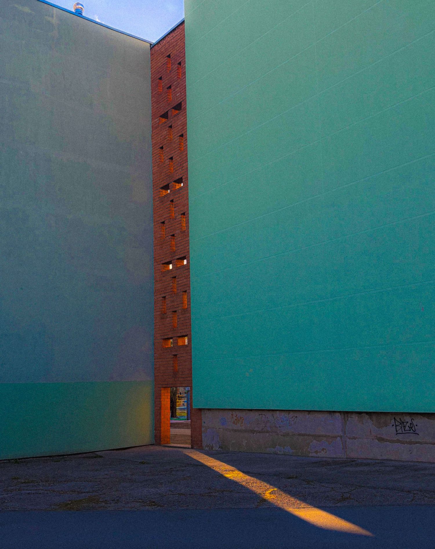 Modern building exterior with teal walls and brick column detail casting golden shadows at dusk.