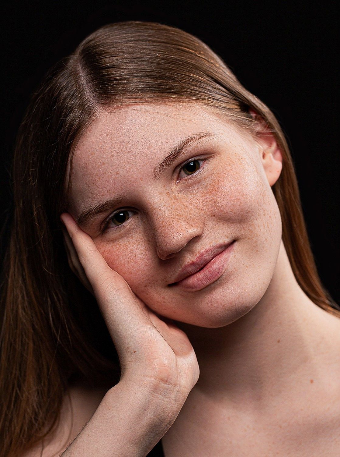 Portrait of a young woman with freckles and long hair resting her chin on her hand.