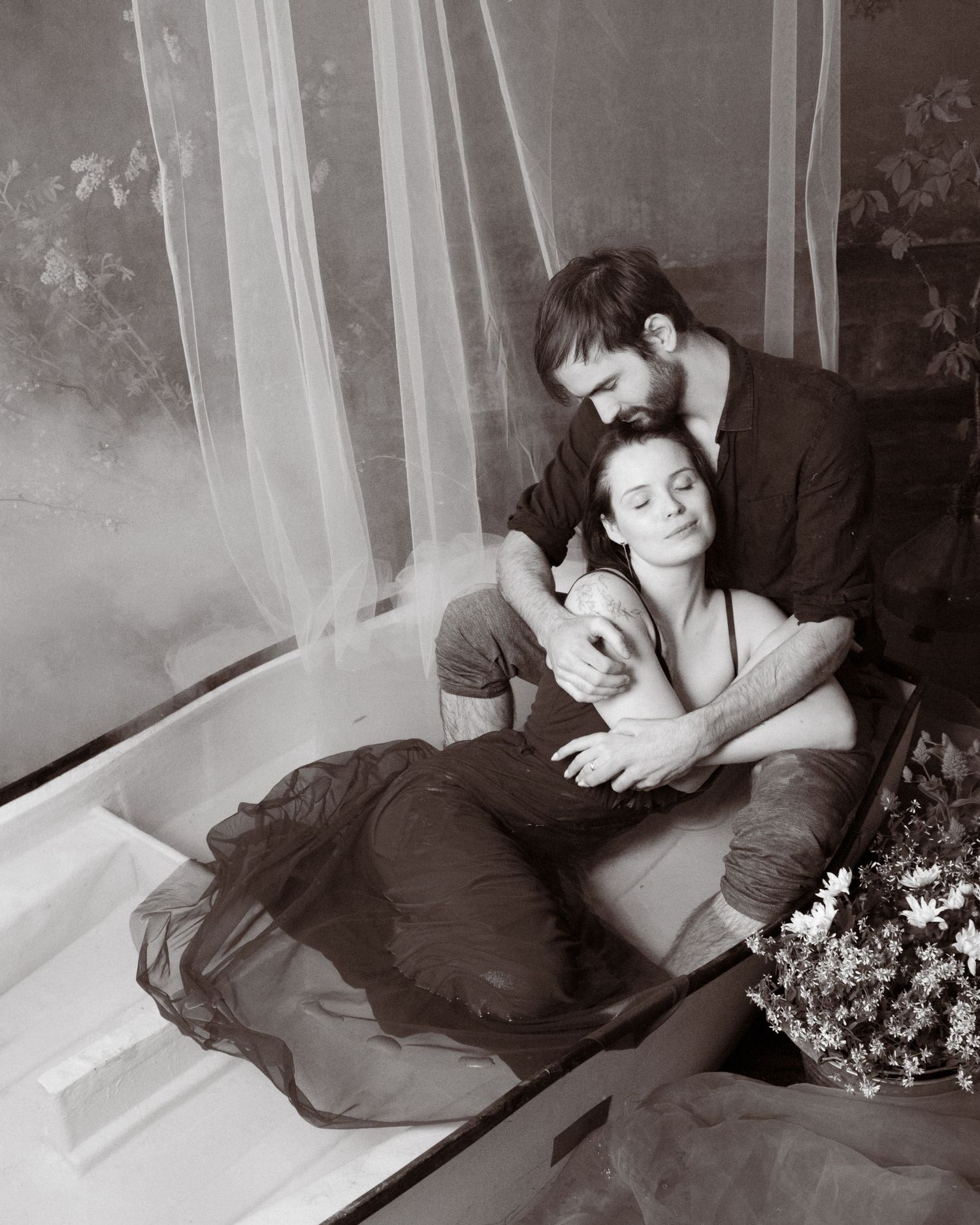 Black and white photo of a couple tenderly holding a newborn baby together in a serene, intimate setting.