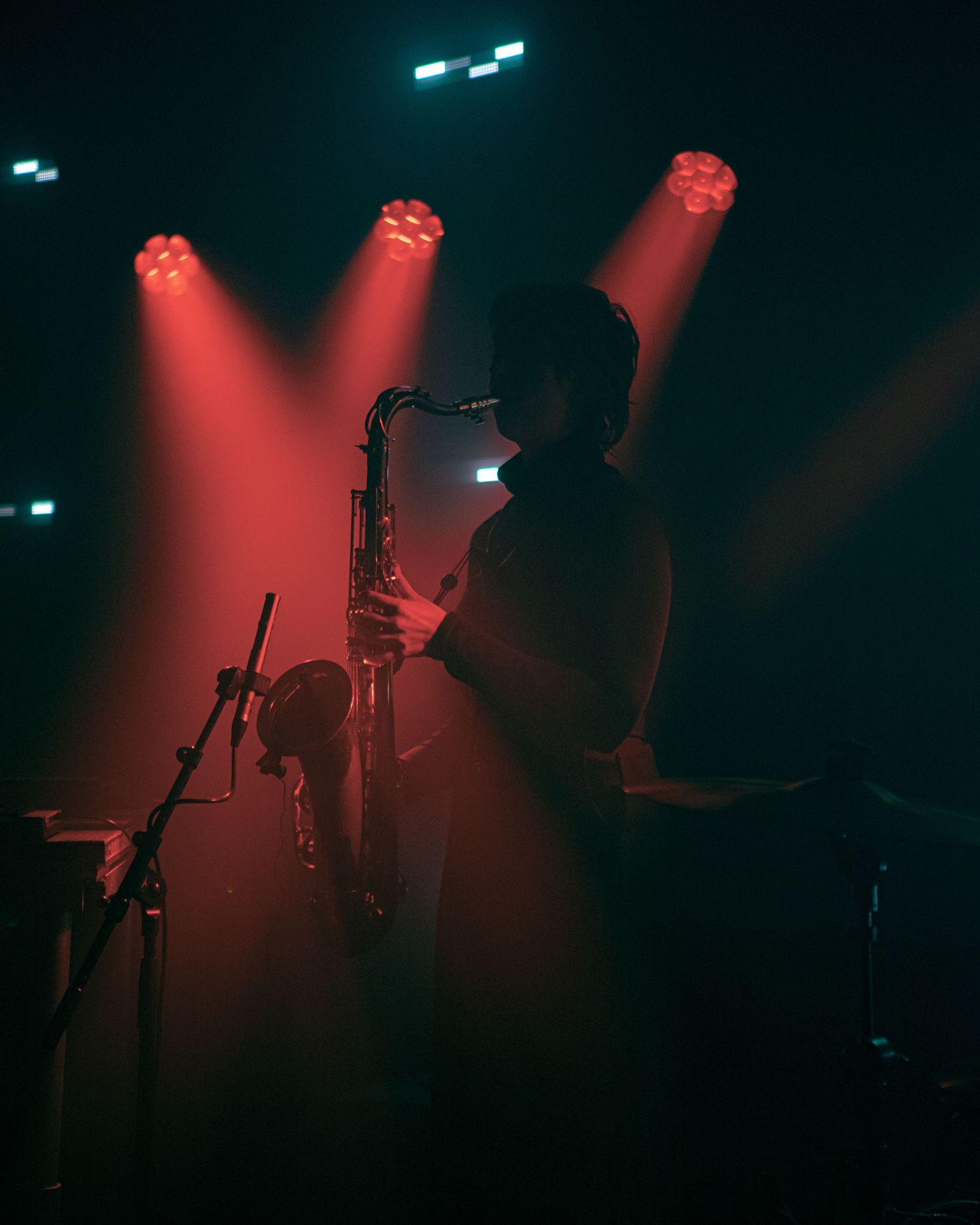 Silhouetted saxophonist performing on stage under dramatic red spotlights in a dark concert venue.