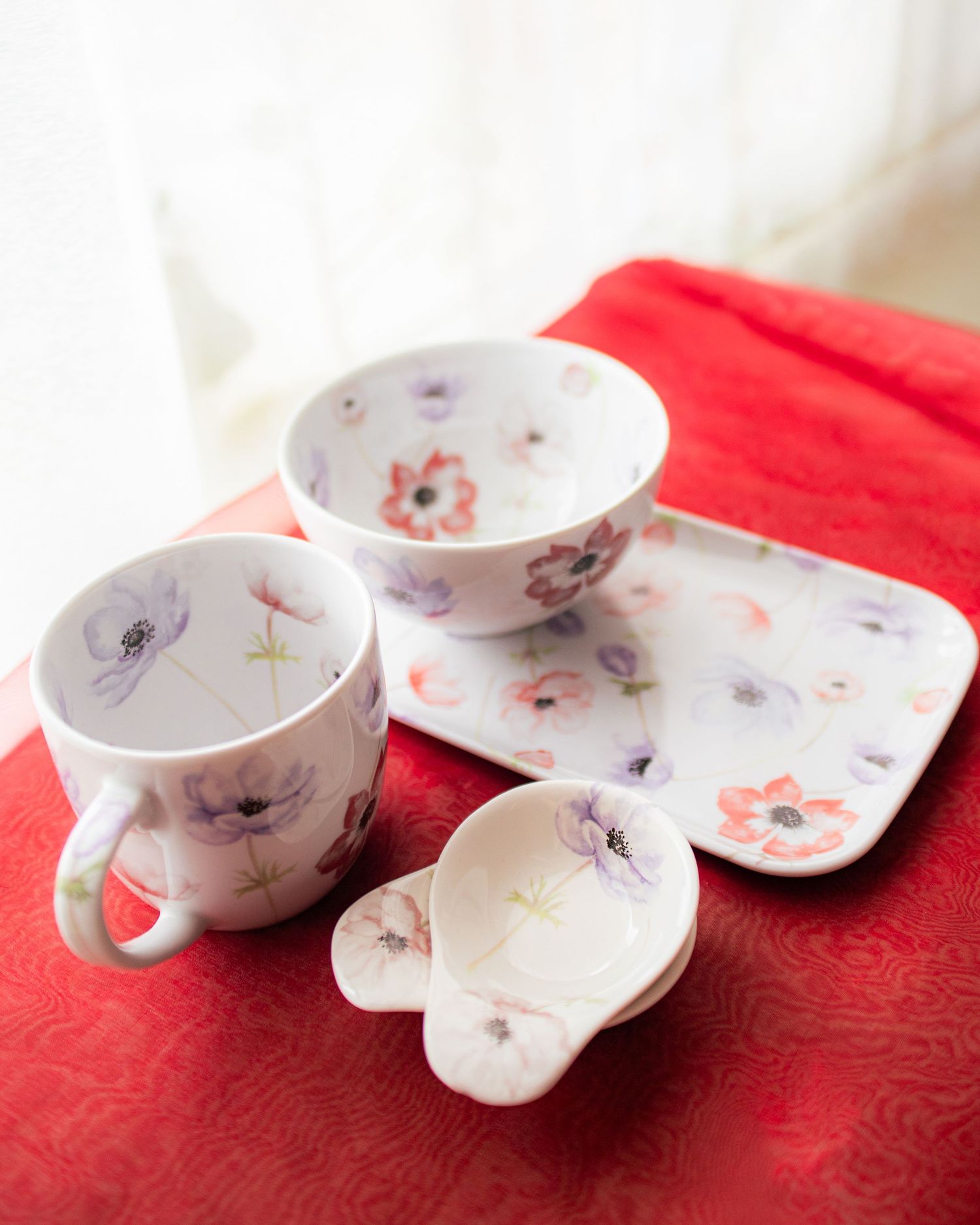 Floral porcelain tea set with cup, bowl, plate, and small dish featuring pink and purple anemone flowers on white.