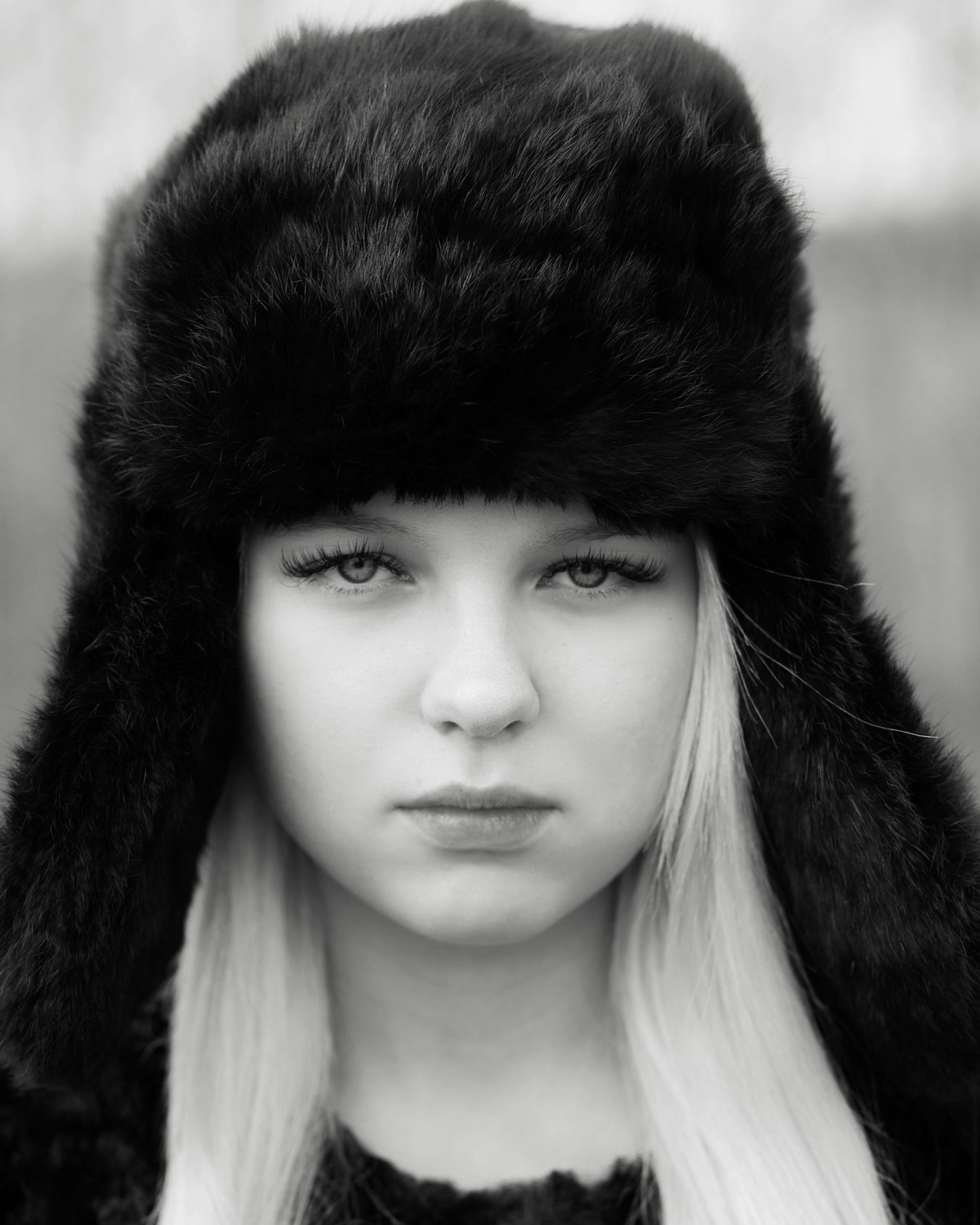 Black and white portrait of a young woman wearing a black fur ushanka hat with long blonde hair.