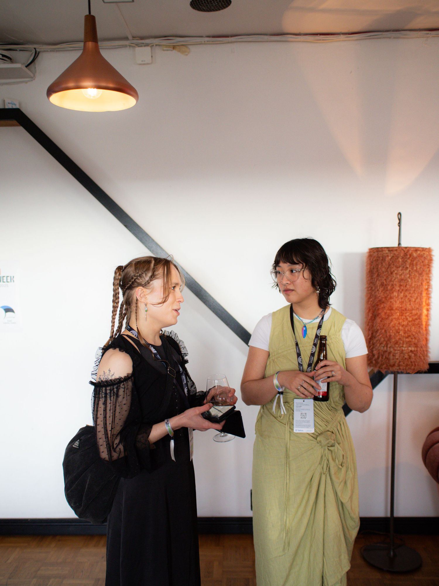 Two women conversing at an art gallery event, one in black lace and one in an olive green outfit.
