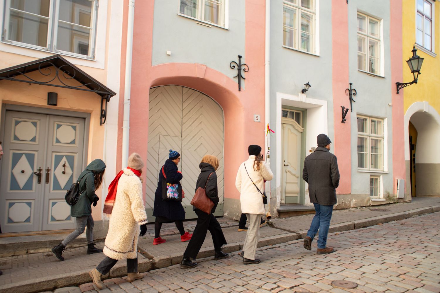 A group of people walk along a cobblestone street past colorful pastel buildings in old town.