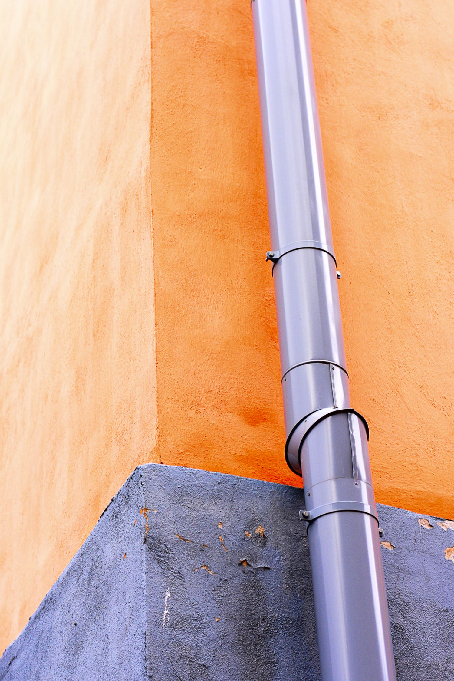 Gray drainpipe mounted on corner of orange and blue painted building exterior wall.