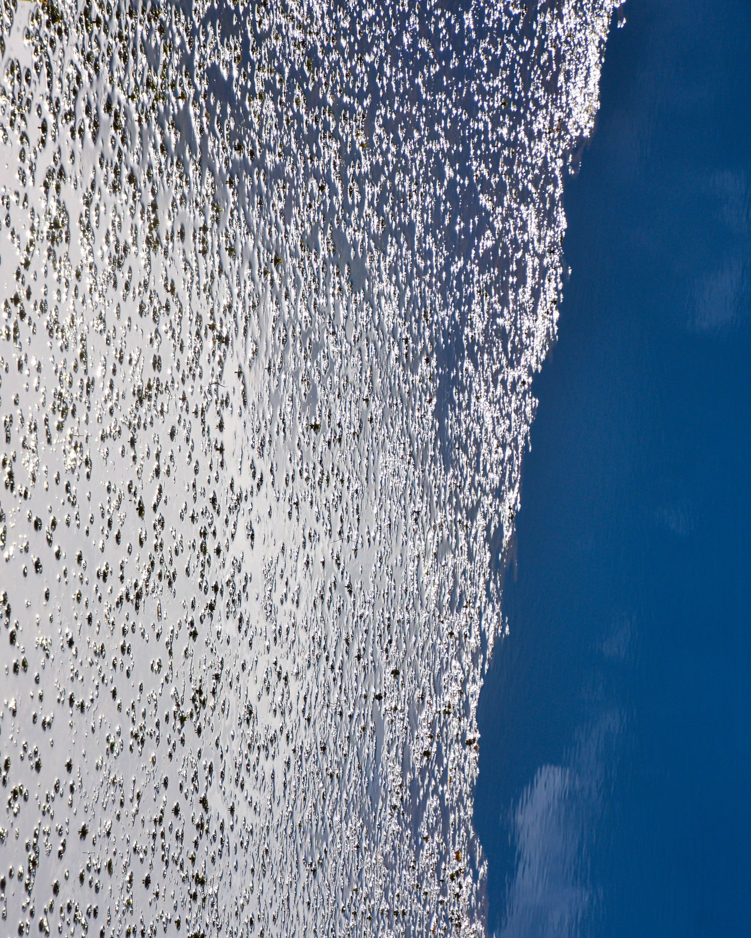 Aerial view of sparkling ocean waves meeting calm blue water along a shoreline.