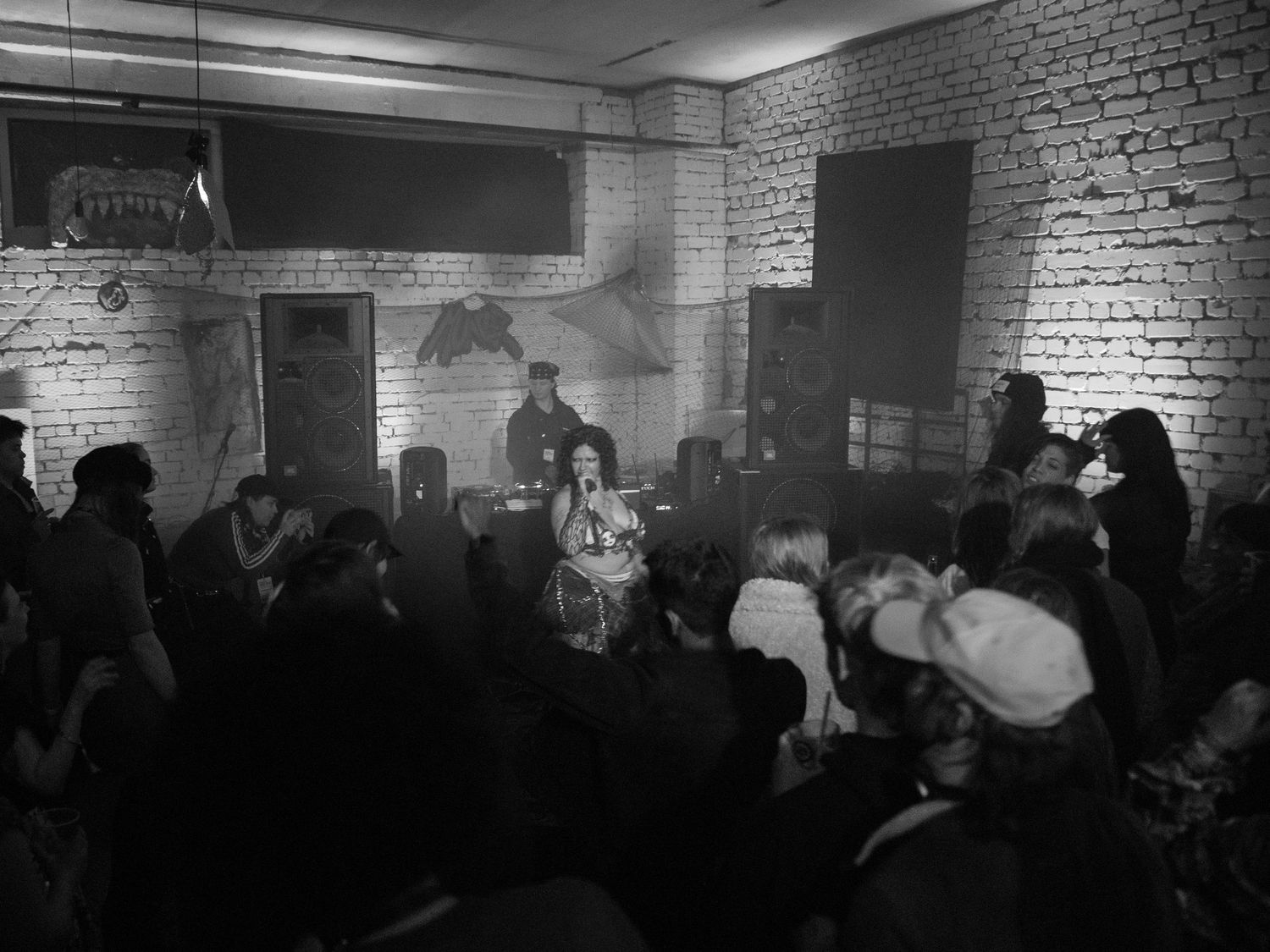 Black and white photo of a live music performance in a brick-walled venue with an intimate crowd gathered.