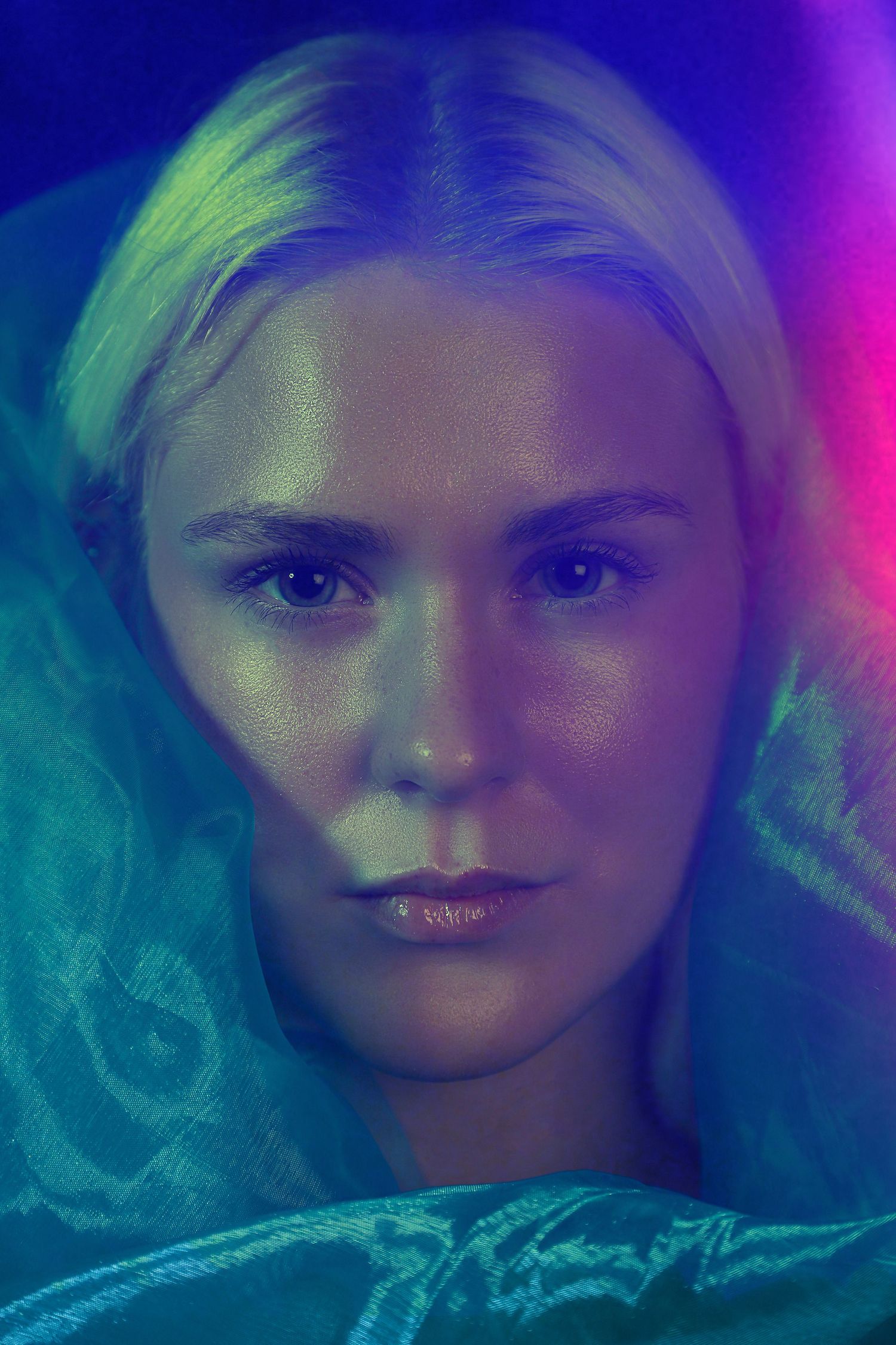 Close-up portrait of blonde woman under blue and pink neon glow.