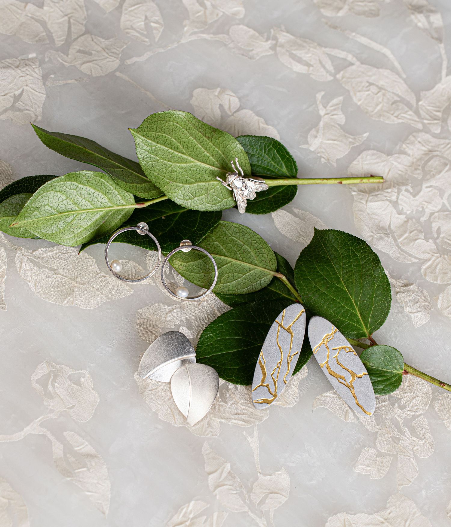 Elegant silver jewelry collection with kintsugi earrings and hoop earrings arranged on green leaves.
