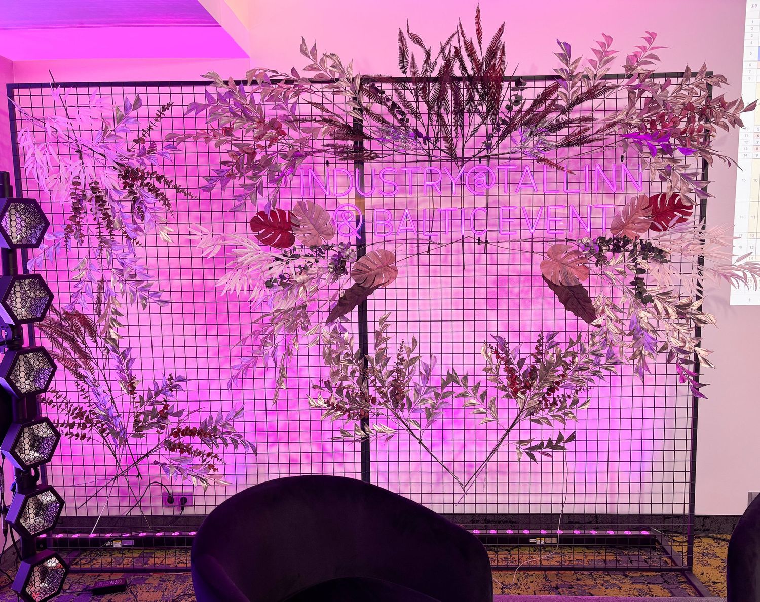 Decorative floral backdrop with pink lighting and tropical leaves for an event photo wall.