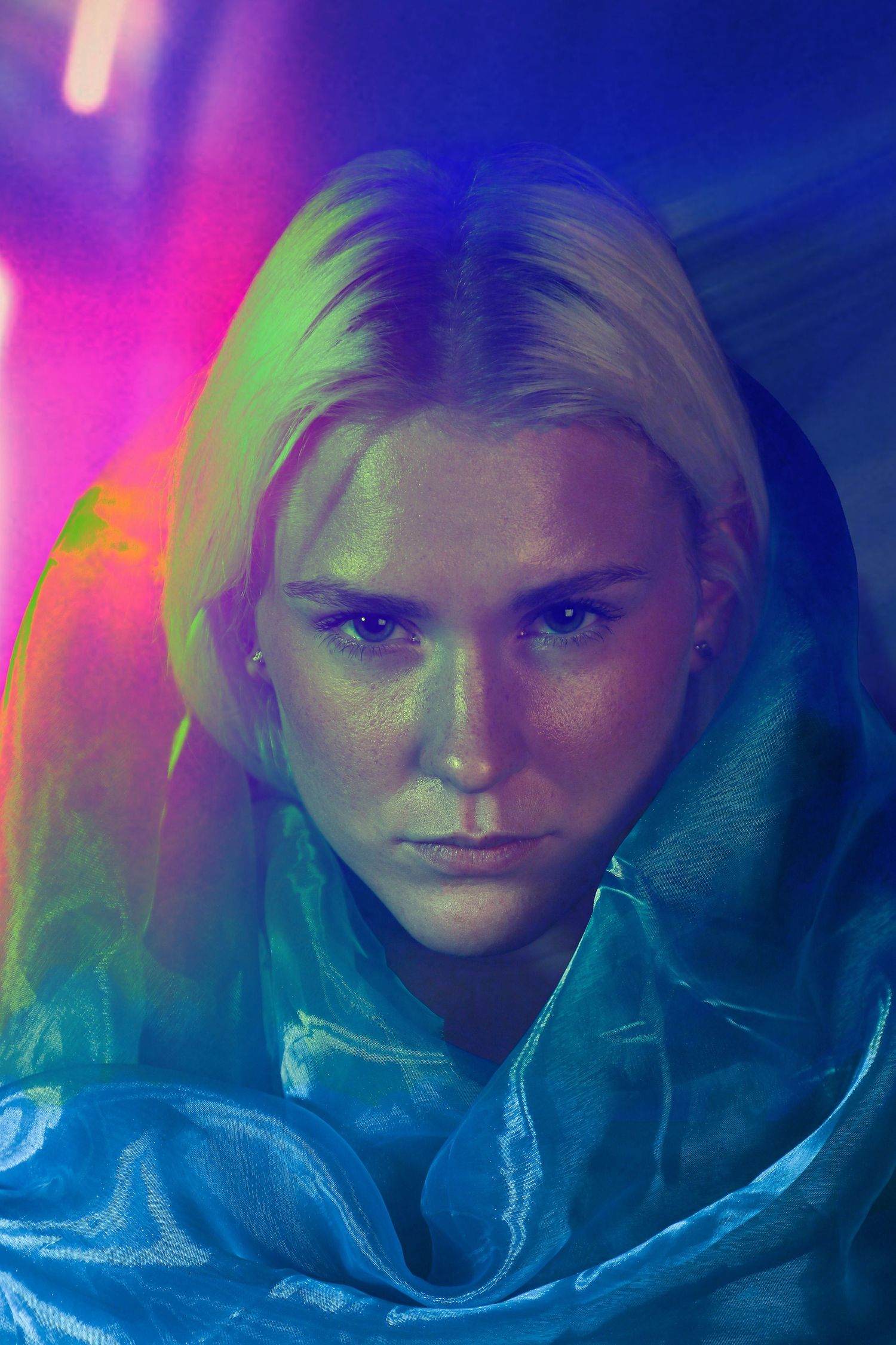 Blonde woman wrapped in teal fabric under colorful neon lights.