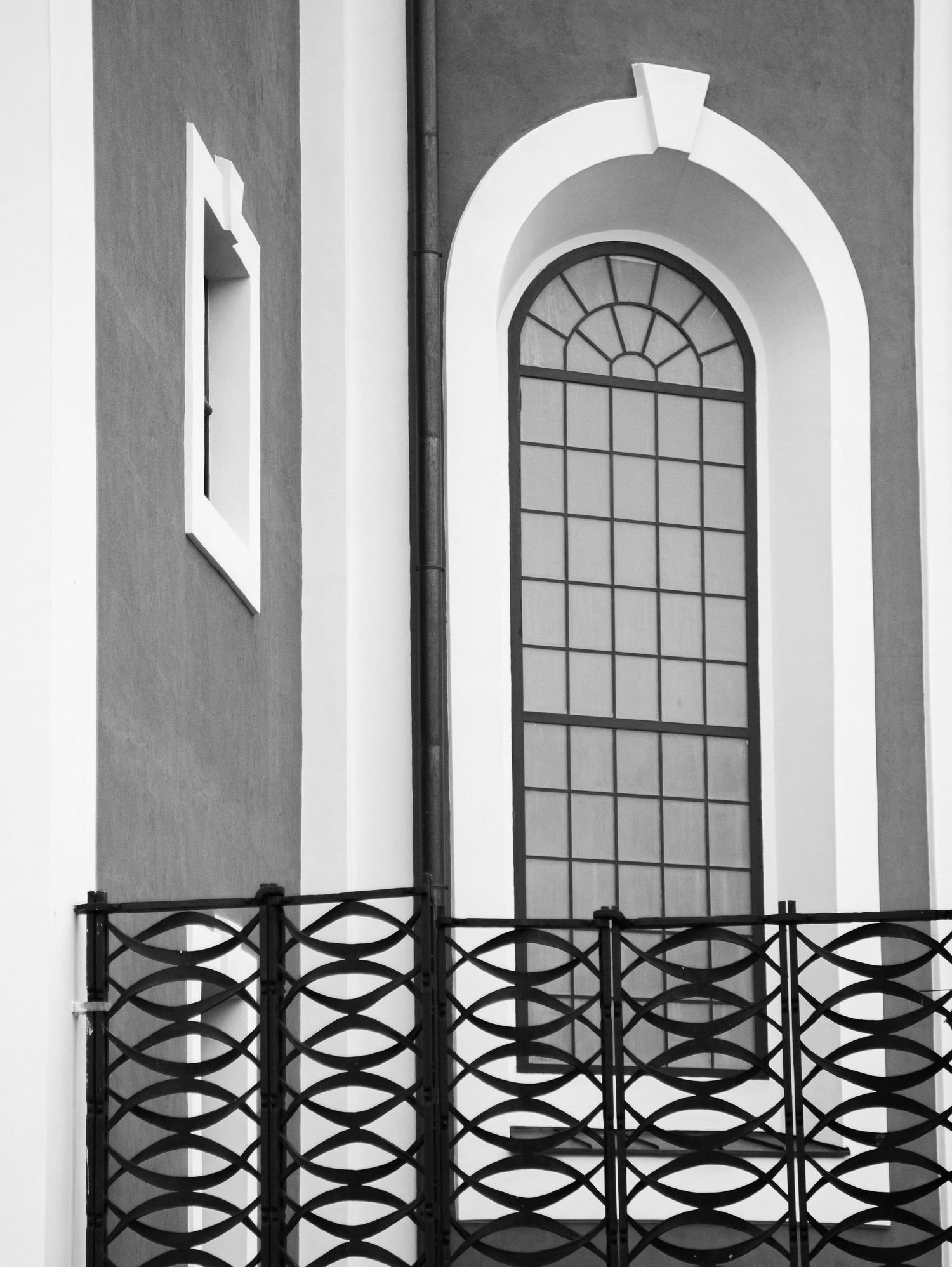Black and white photo of a tall arched church window with iron railings and decorative metalwork.