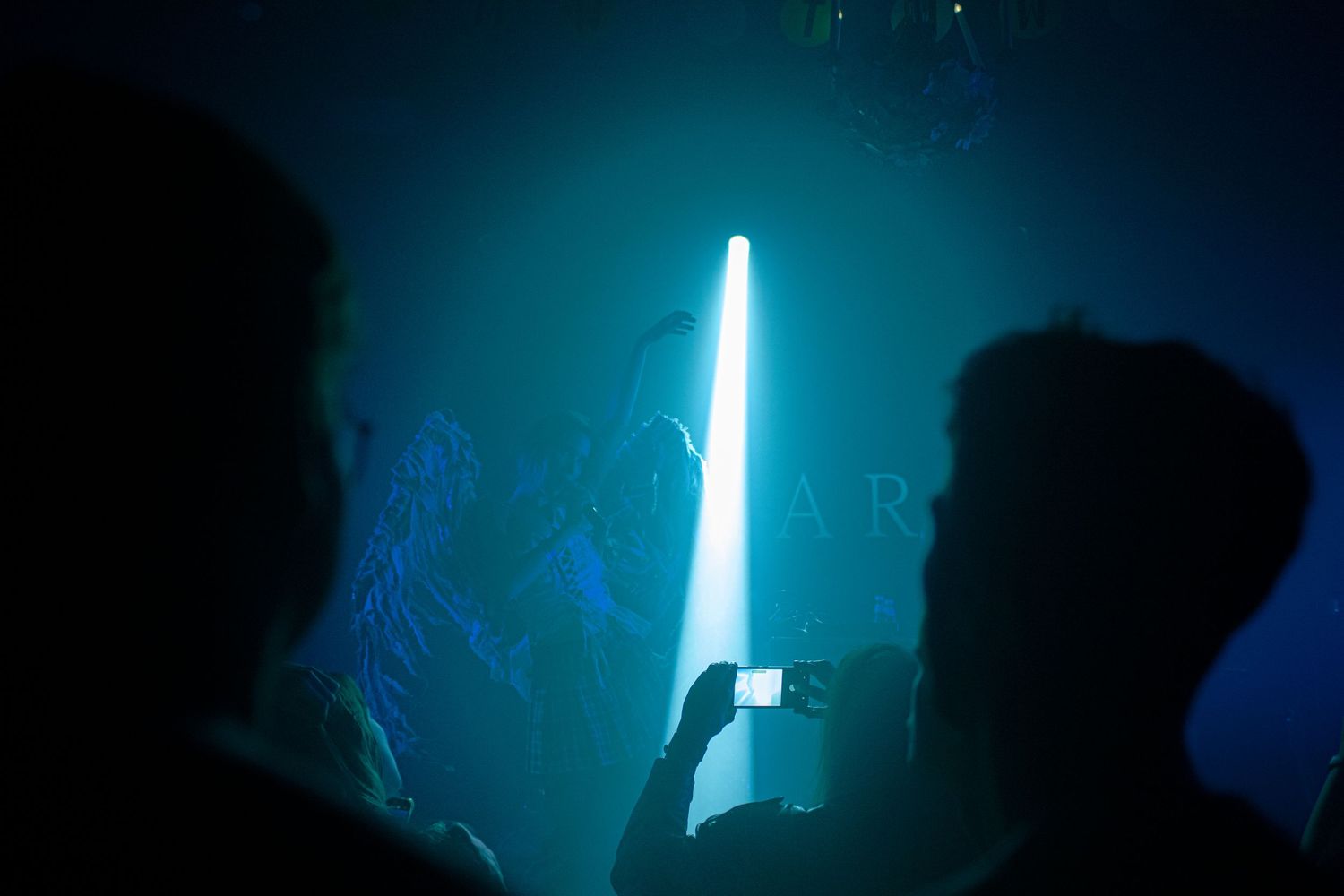 Silhouetted crowd at a nightclub with a bright blue spotlight beam cutting through smoky atmosphere.